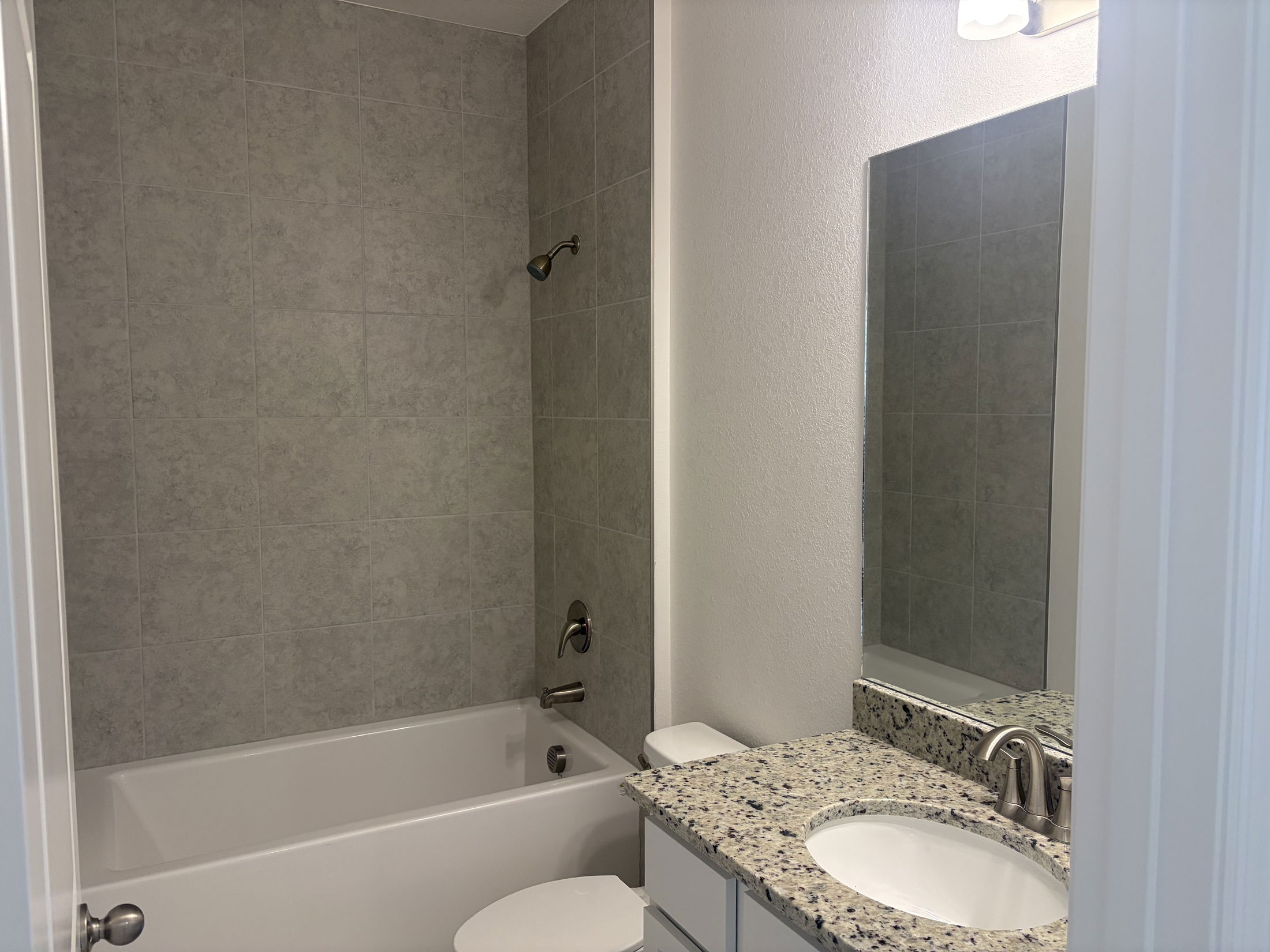 Modern bathroom featuring a tub, granite countertop sink, and neutral tile walls.
