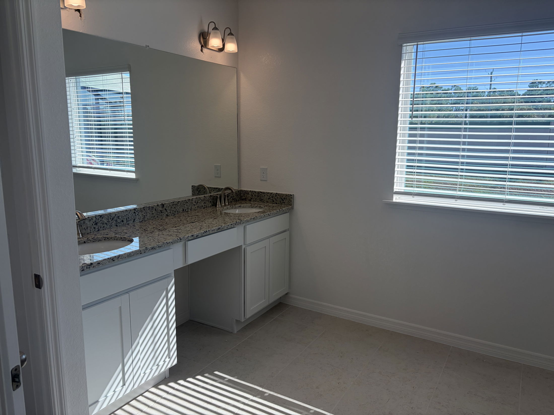 Bright and spacious bathroom featuring a granite countertop double vanity and natural light from a nearby window.