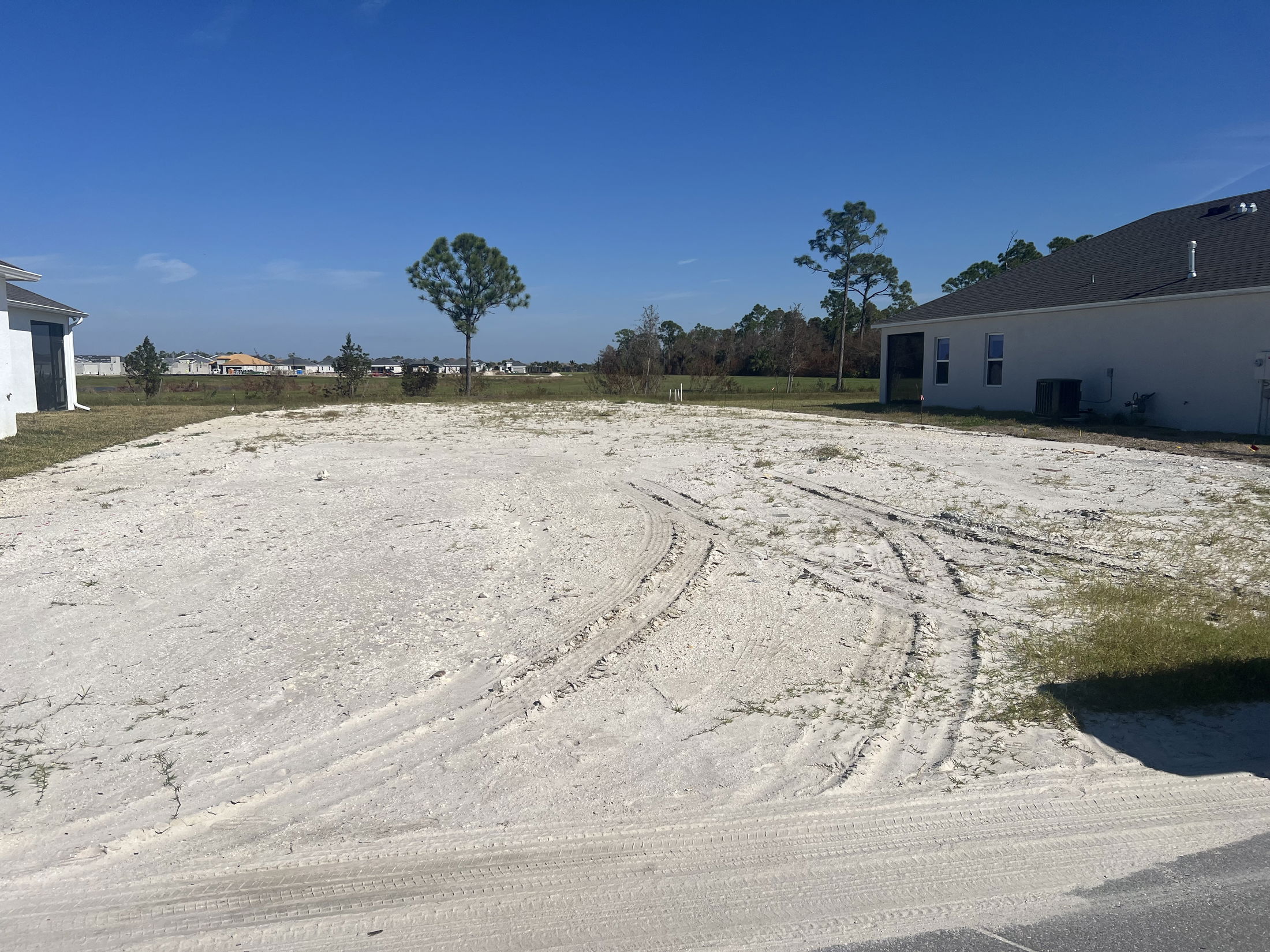 Empty sandy lot between two houses in a residential area under a clear blue sky.