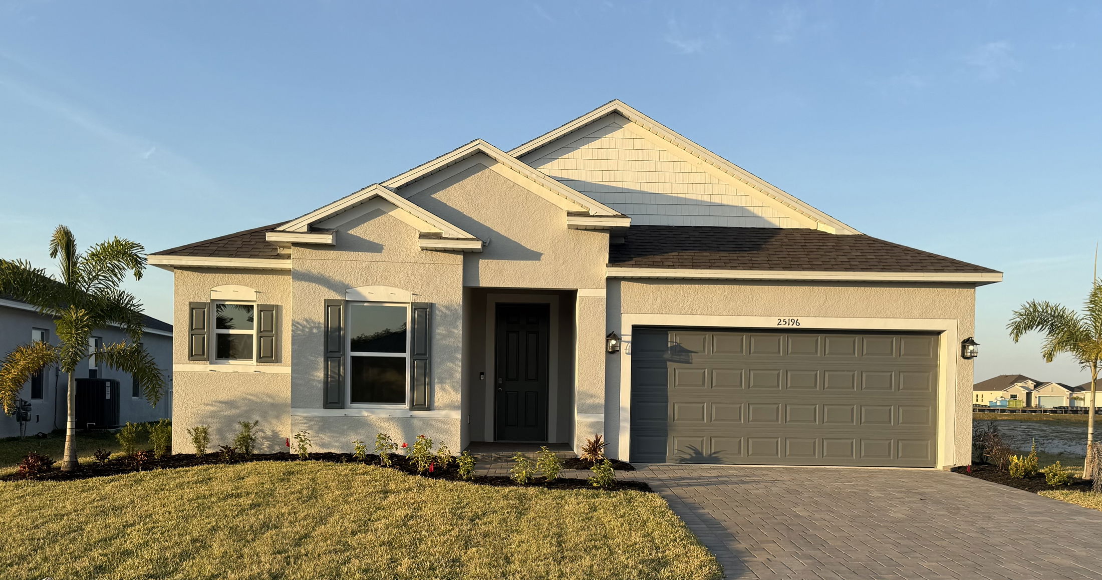 Newly constructed single-story home with a manicured lawn, palm trees, and a two-car garage.
