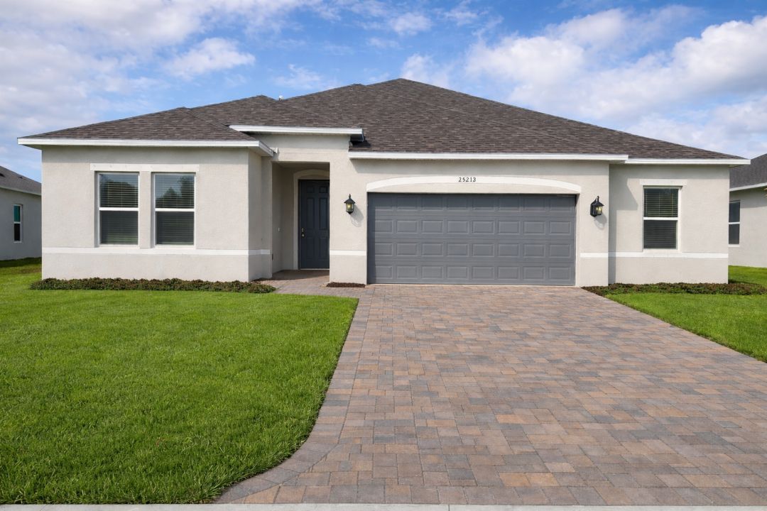 Modern residential home with a gray garage door, well-maintained lawn, and brick driveway under a blue sky.