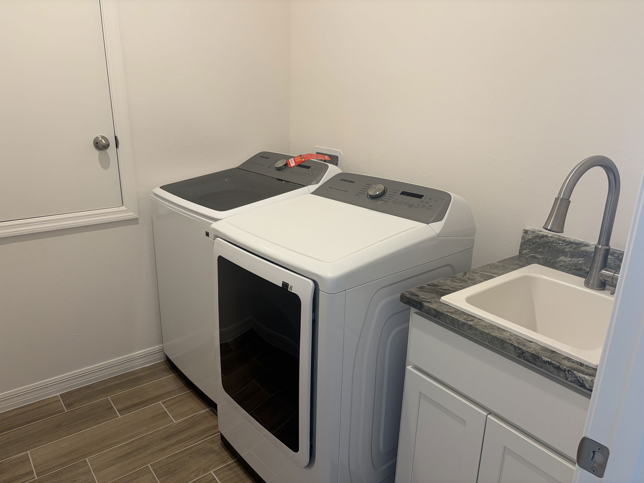 A modern laundry room featuring a washing machine, dryer, and a utility sink with gray countertops.
