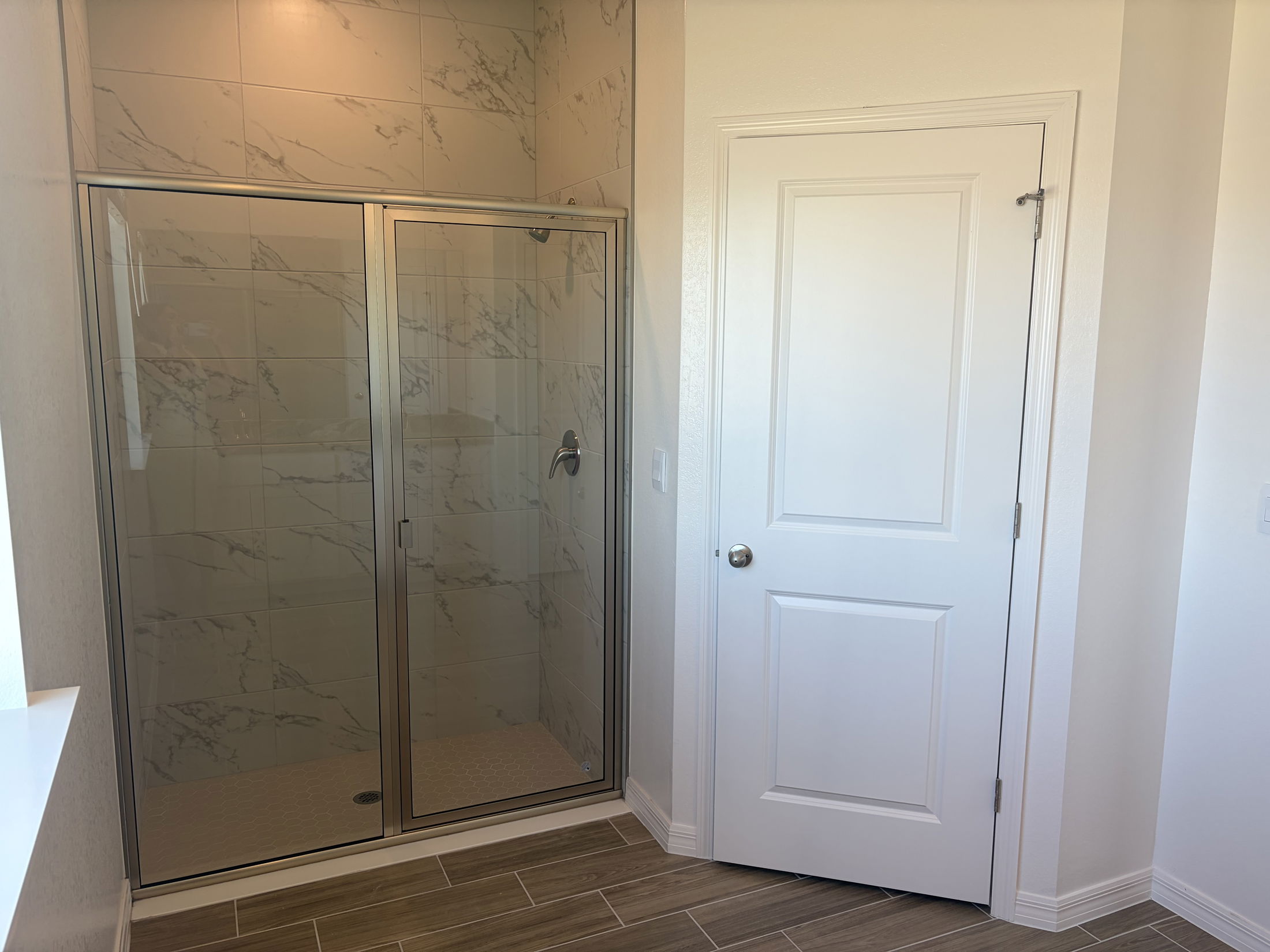 Modern bathroom featuring a glass shower enclosure with marble tiles and a white door.