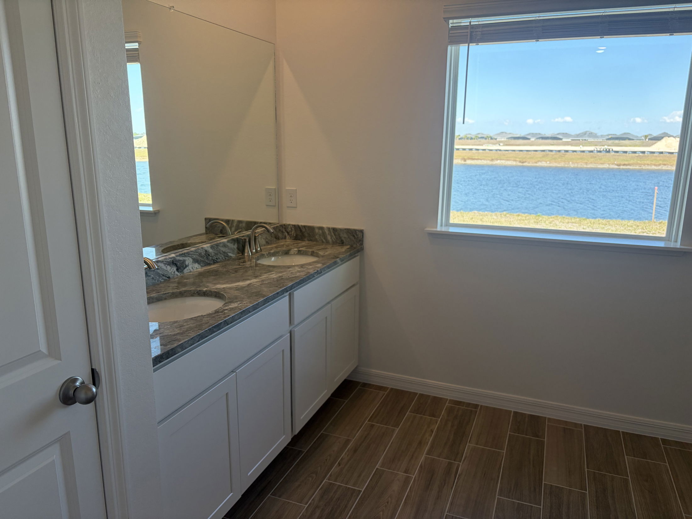 Modern bathroom with dual sinks, granite countertop, and a large window overlooking a scenic water view.