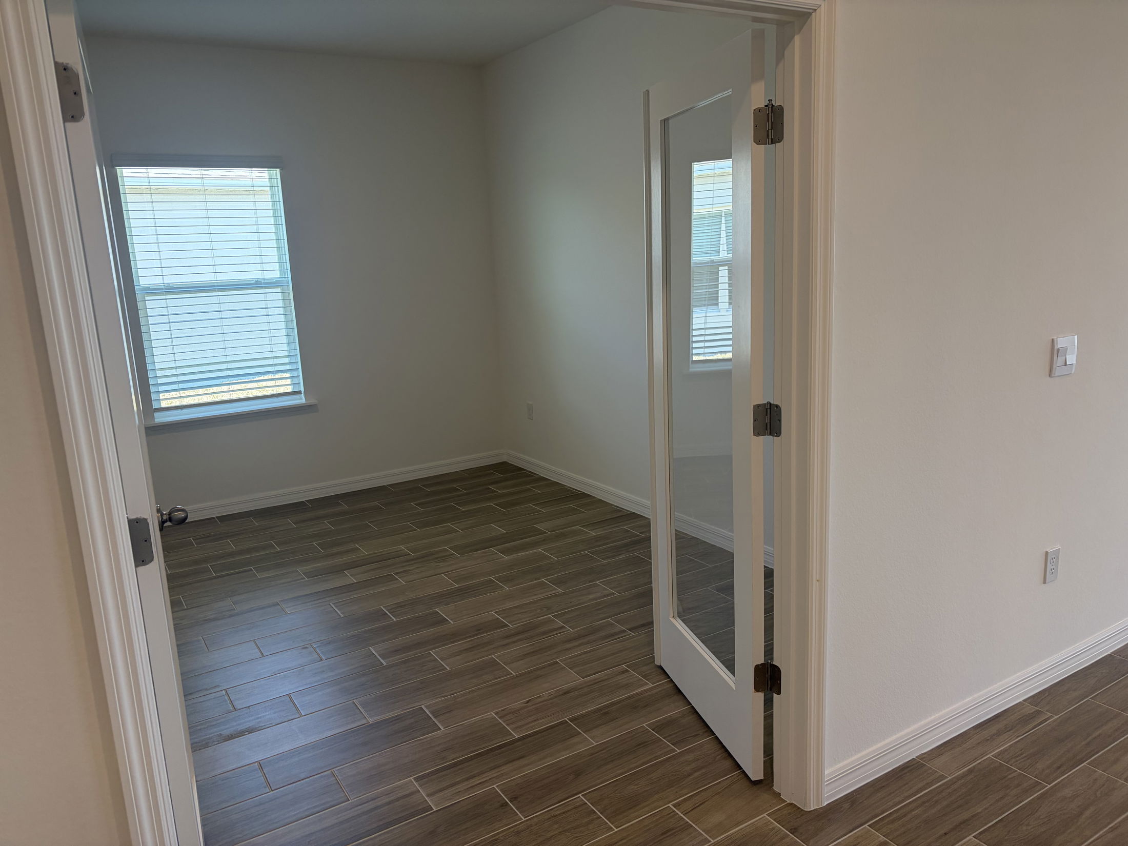 Bright and spacious room featuring large window and modern tile flooring in a newly constructed home.