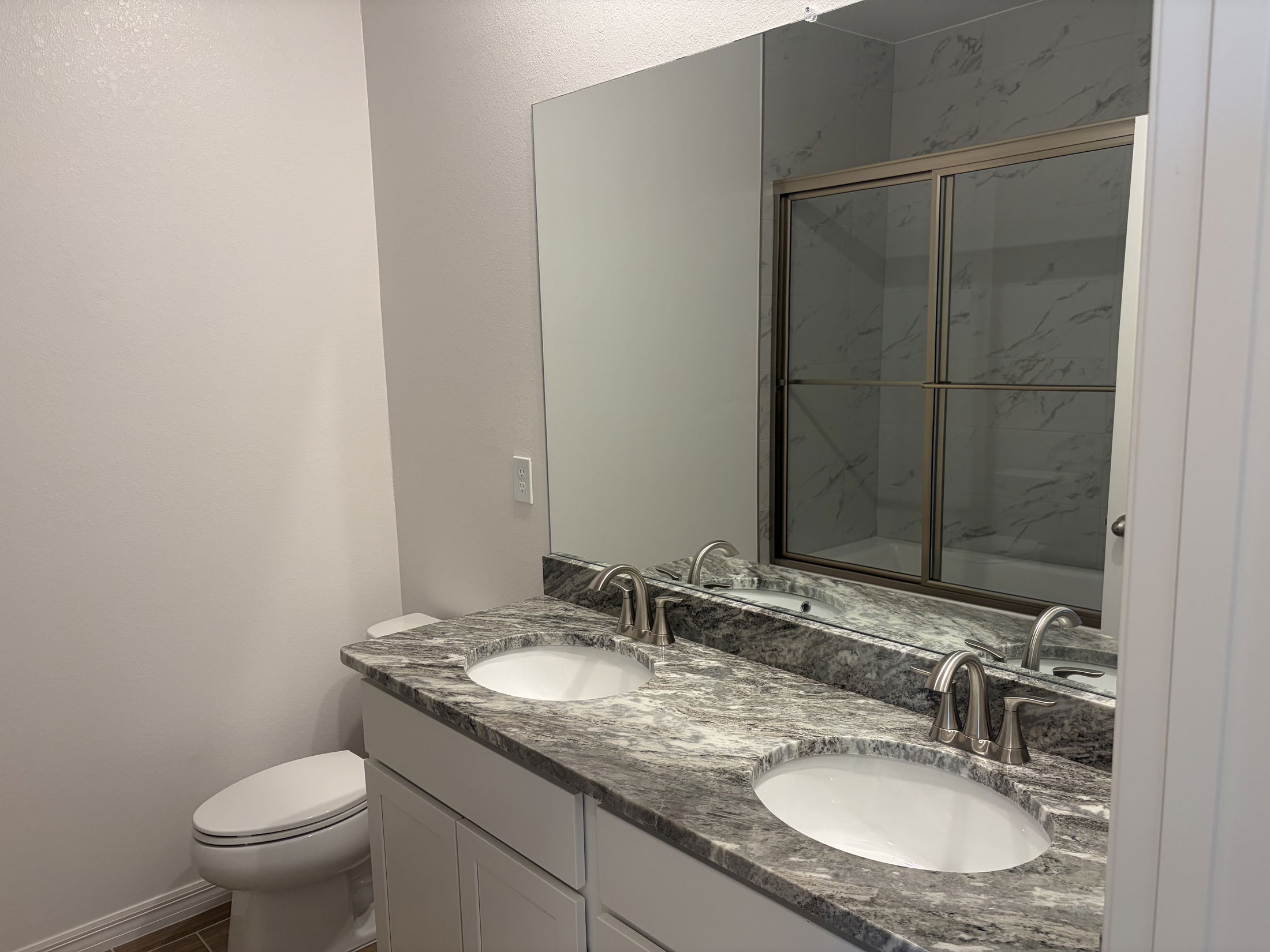 Modern bathroom featuring a dual-sink vanity with granite countertops, a mirror, and a shower enclosure.