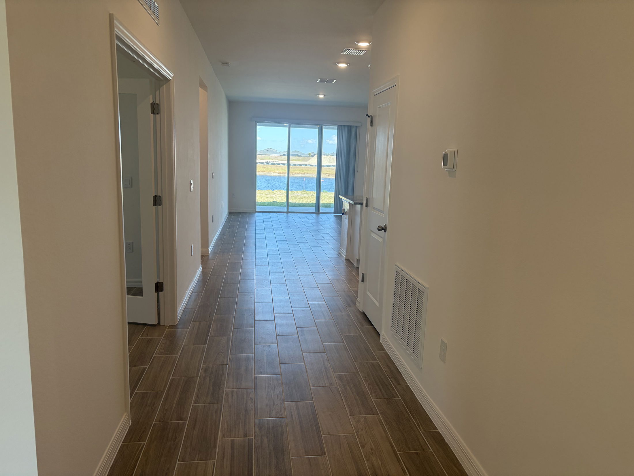 Bright and modern hallway leading to a spacious living area with large windows overlooking a scenic landscape.