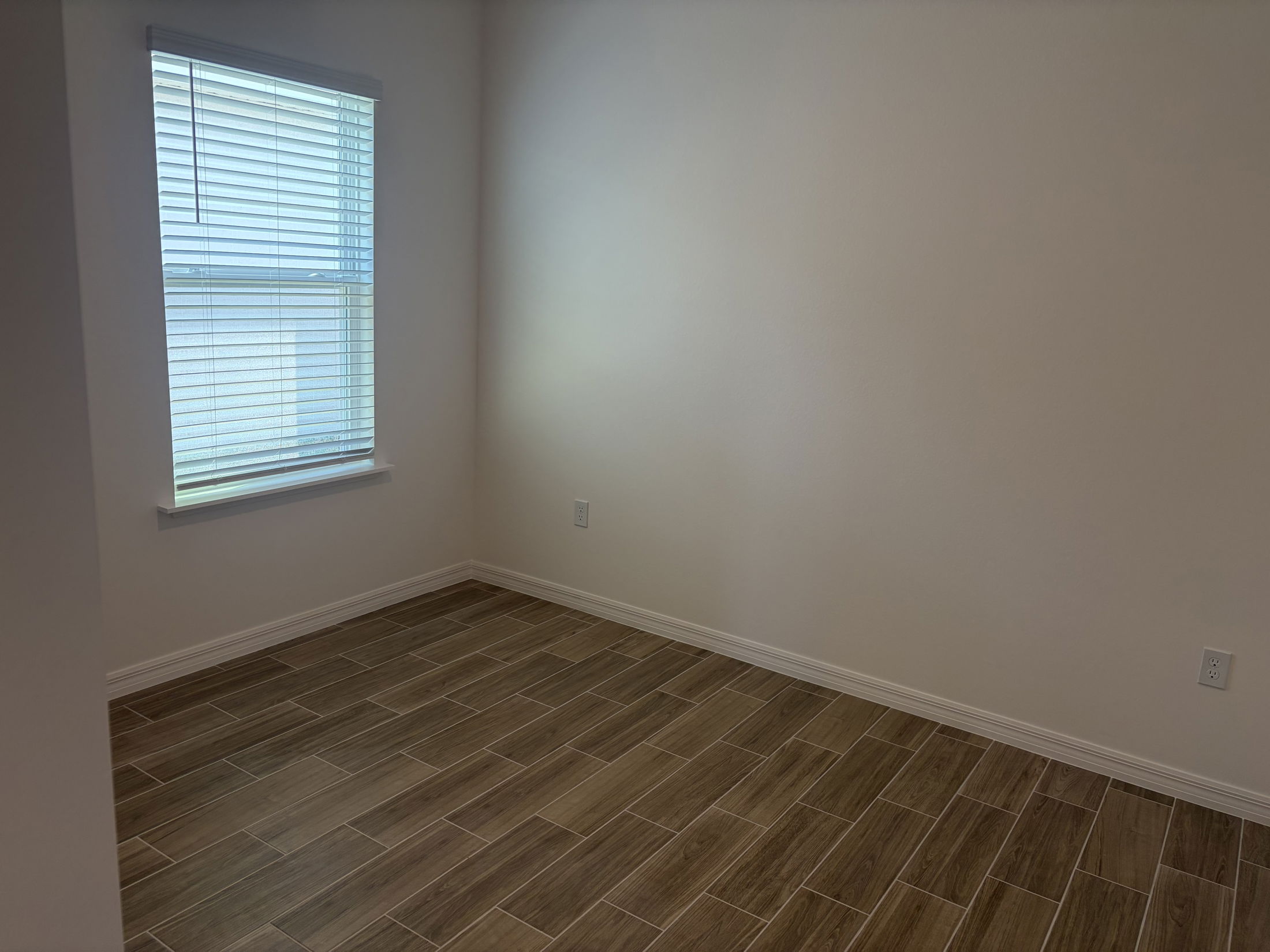 Bright and minimalistic empty room with wooden tile flooring and a window featuring white blinds.