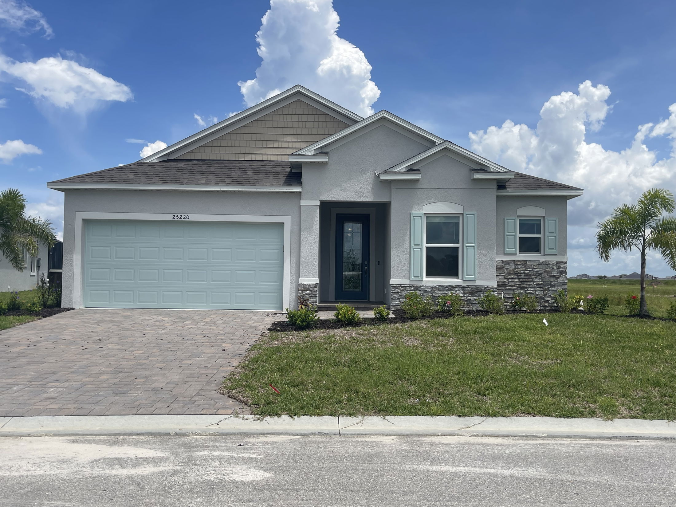 Modern single-story home with a two-car garage, gray stone accents, and neatly landscaped lawn under a clear blue sky.