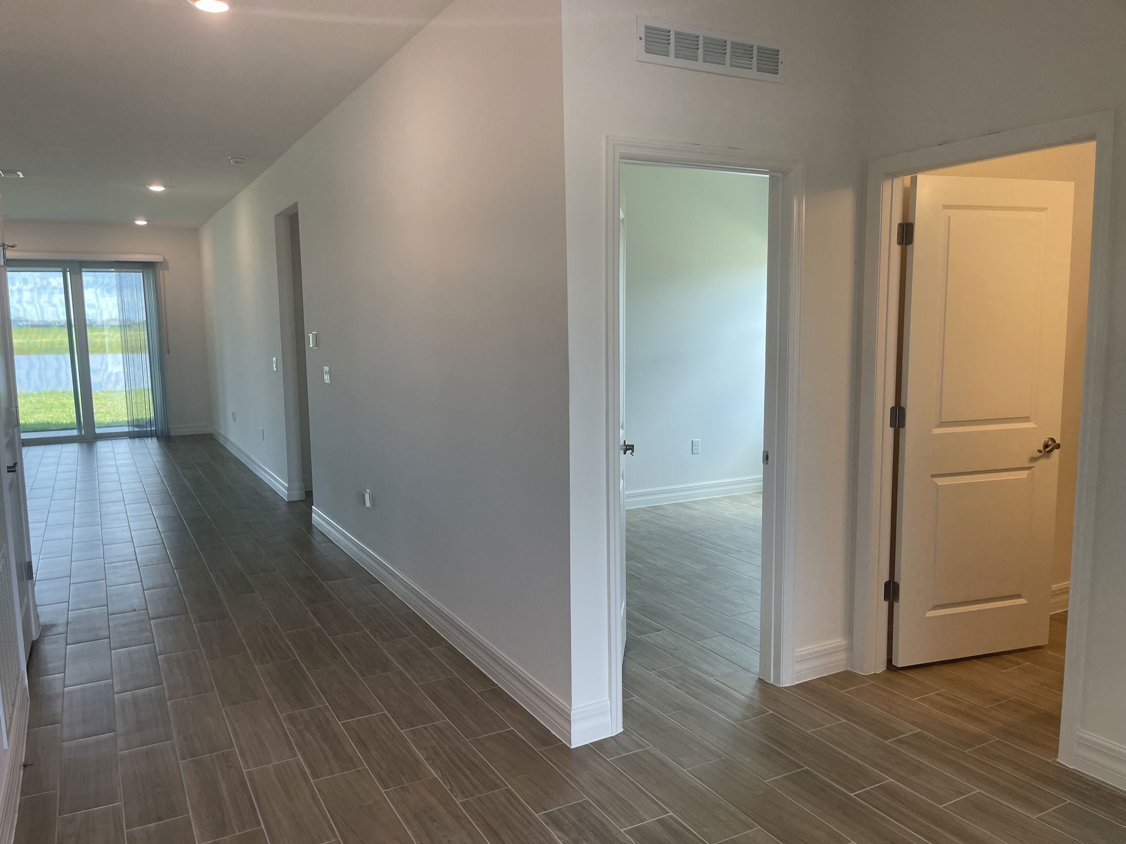 A modern hallway with tile flooring, white walls, and an open door leading to a room with natural light streaming through glass patio doors.