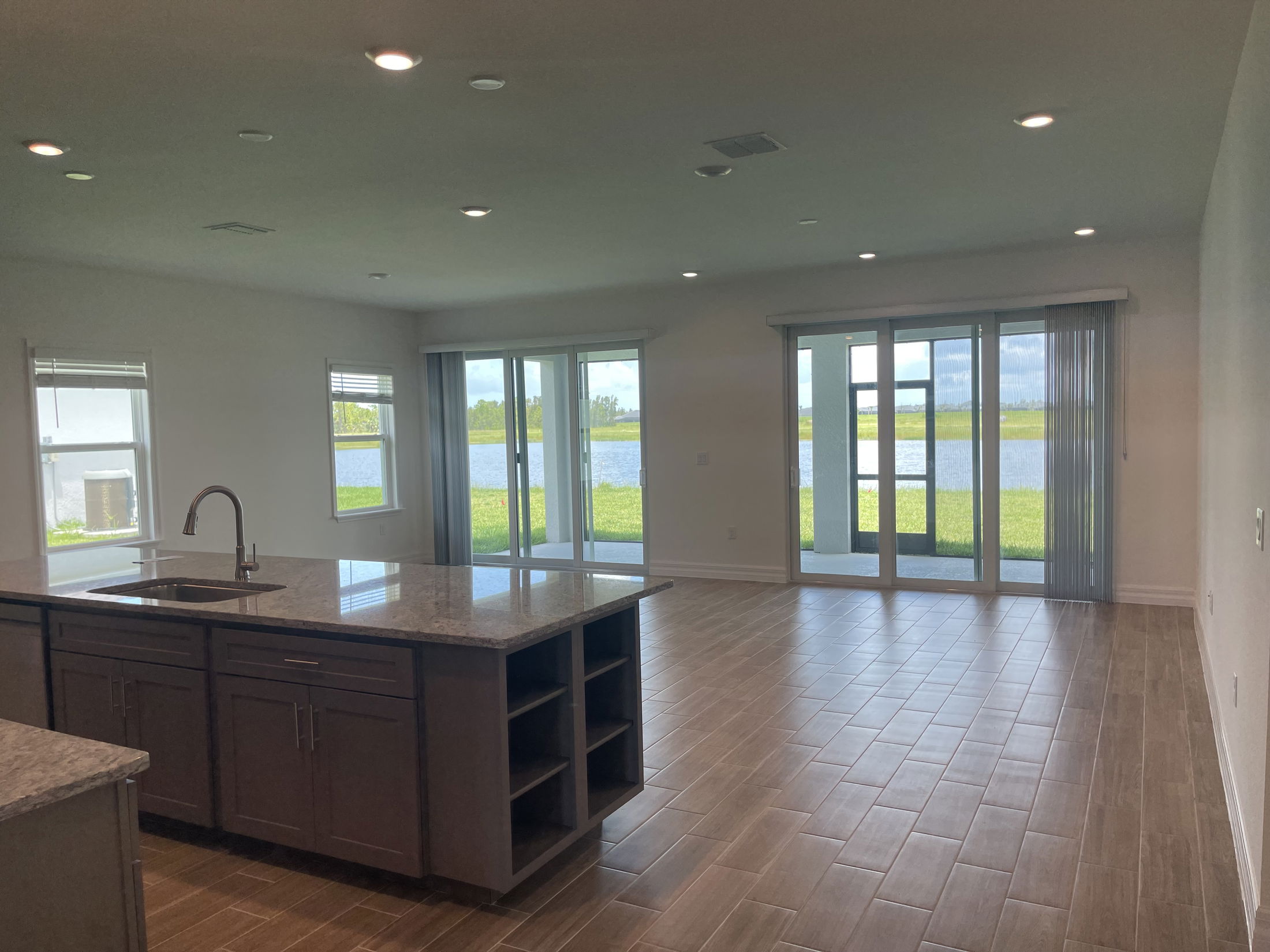 Modern open-plan living area with kitchen island, tile flooring, and large windows showcasing a scenic lake view.