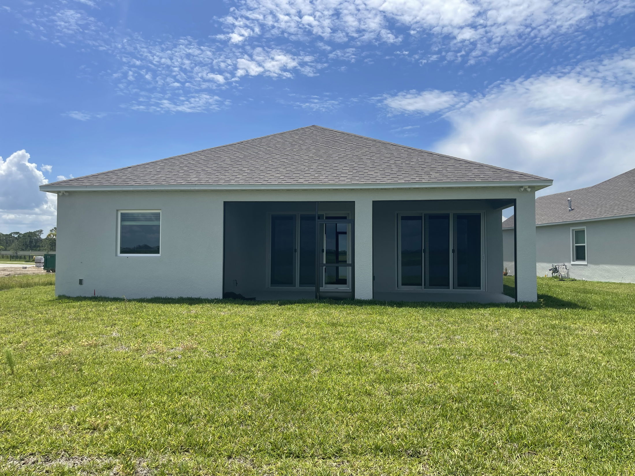 Rear view of a modern suburban house with a spacious backyard and covered patio under a clear blue sky.