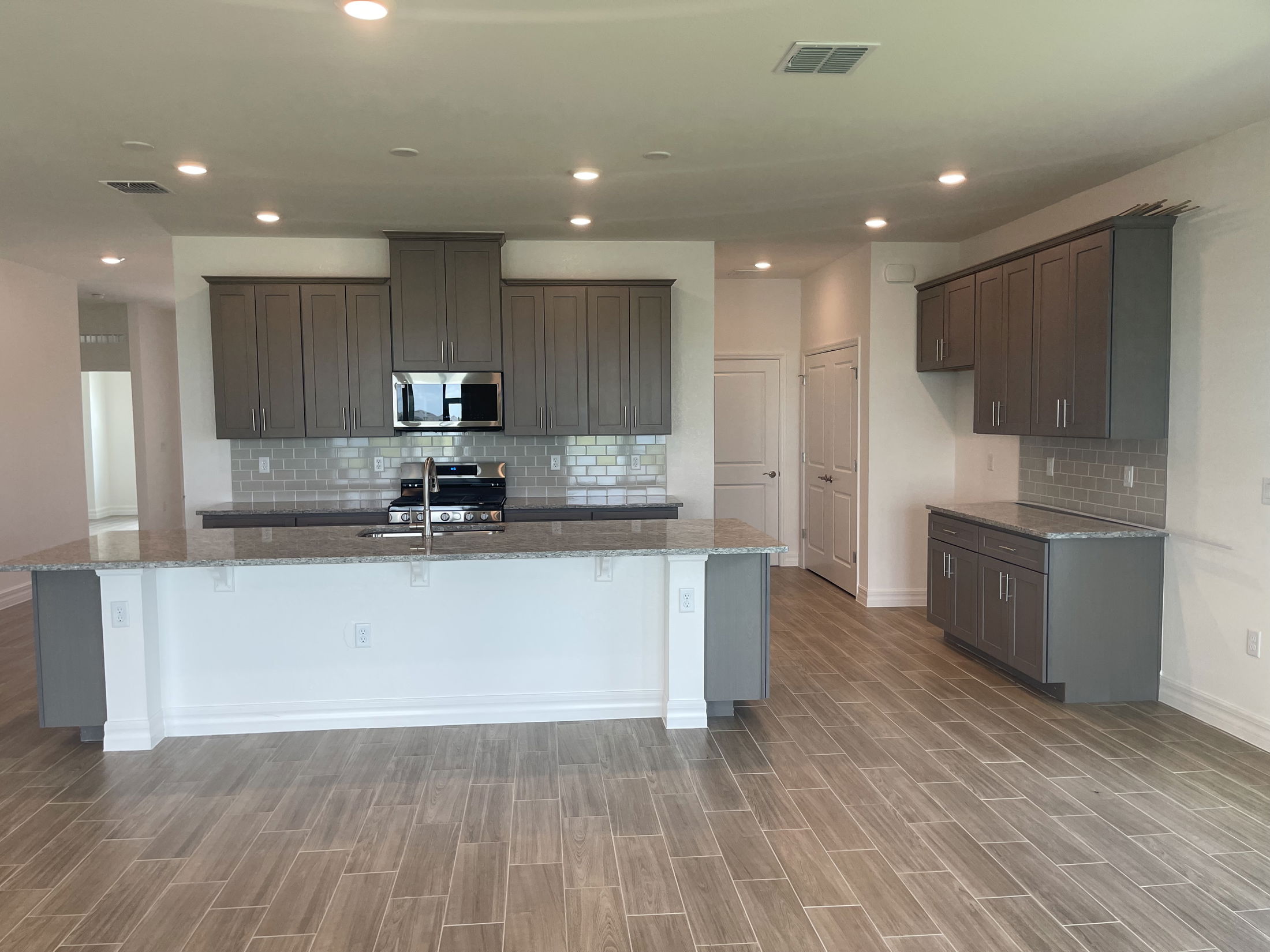 Modern kitchen with gray cabinets, granite countertops, and a center island featuring a built-in sink and stainless steel appliances.