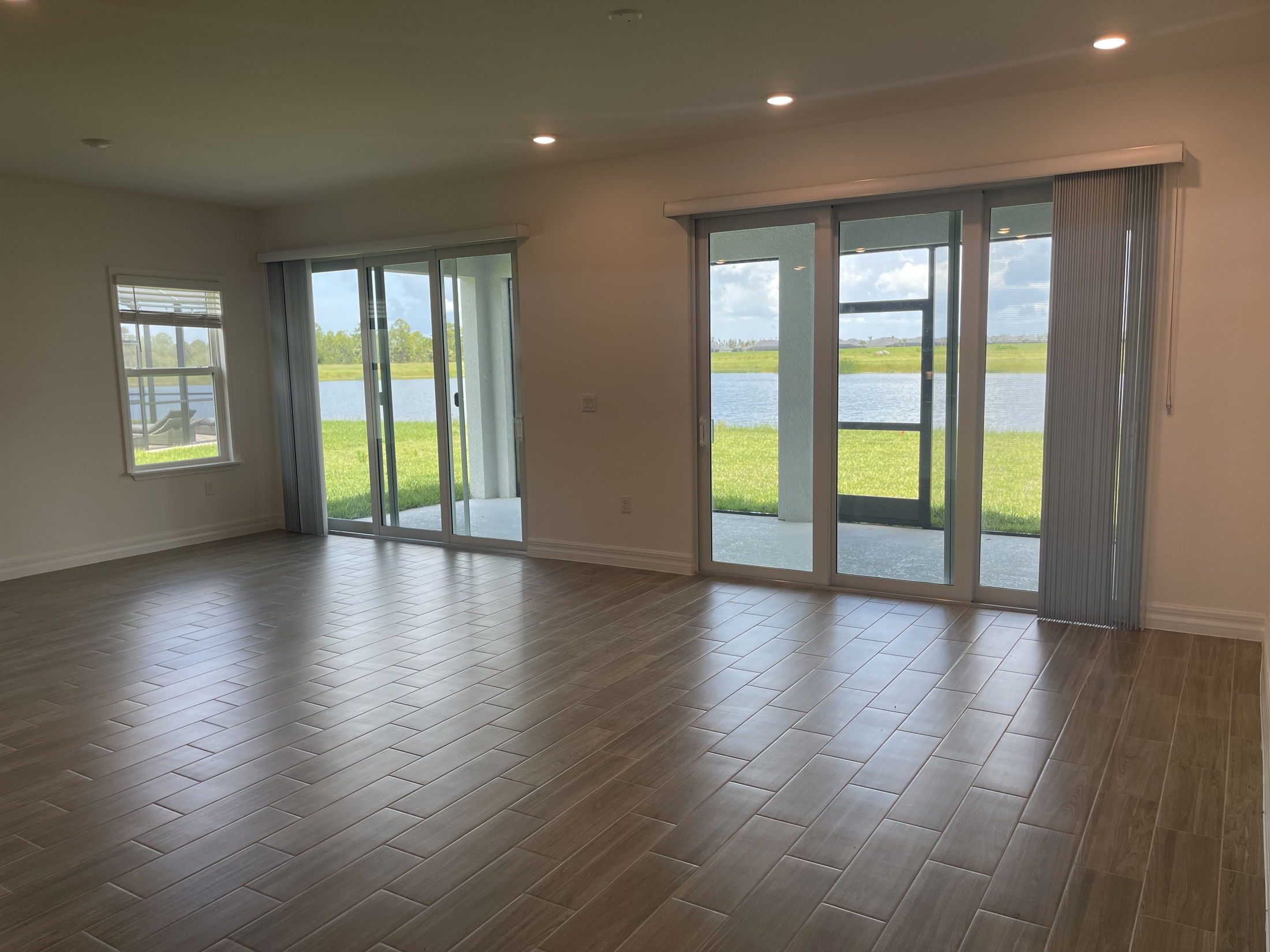 Spacious living room with wood-look tile flooring, large sliding glass doors, and a serene lake view.