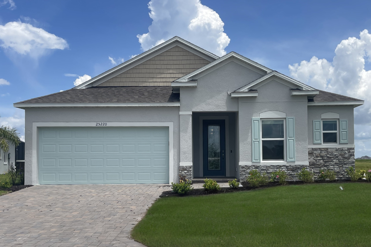 Modern single-story home with stone accents, light blue garage door, and manicured lawn under a blue sky with fluffy clouds.
