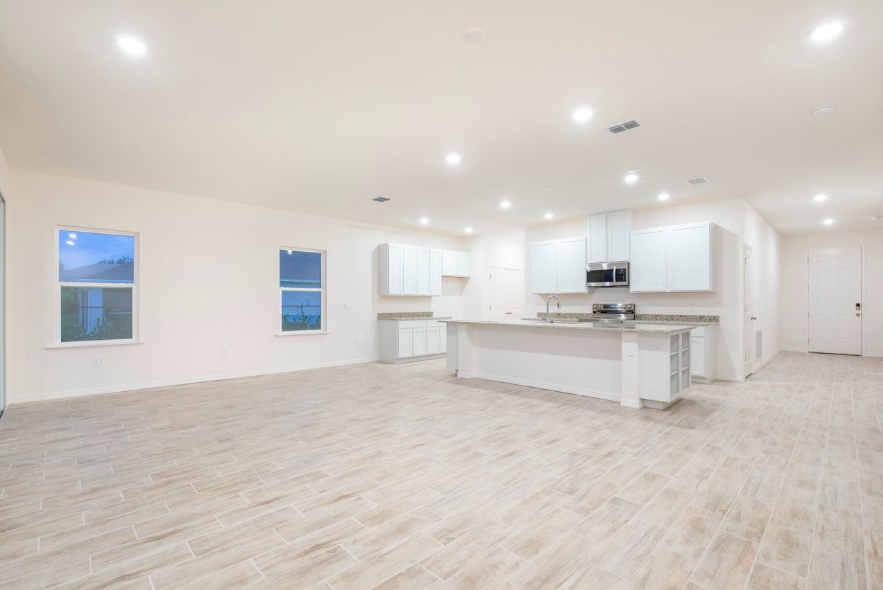 Spacious modern kitchen and living area with light-colored cabinets and tiled flooring in a newly built home.