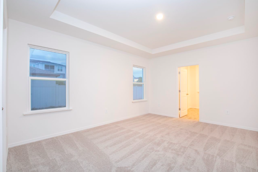 Spacious and well-lit empty bedroom featuring two windows and a doorway leading to a bathroom.