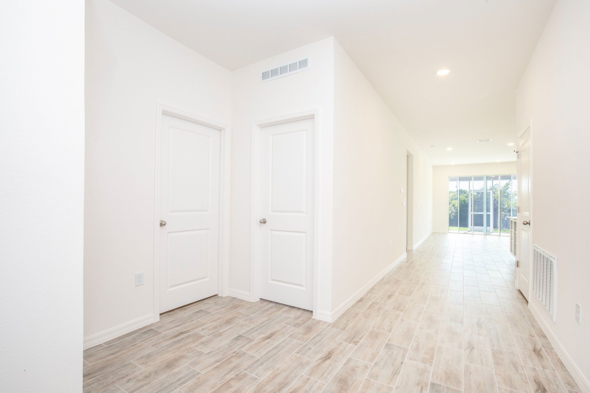 Bright and spacious hallway featuring white walls, multiple doors, and ceramic tile flooring in a modern home.