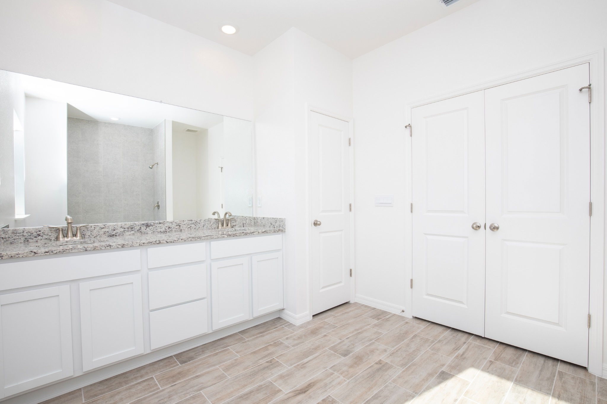 Modern bathroom interior featuring a spacious double sink vanity with granite countertop, large mirror, and stylish tile flooring.