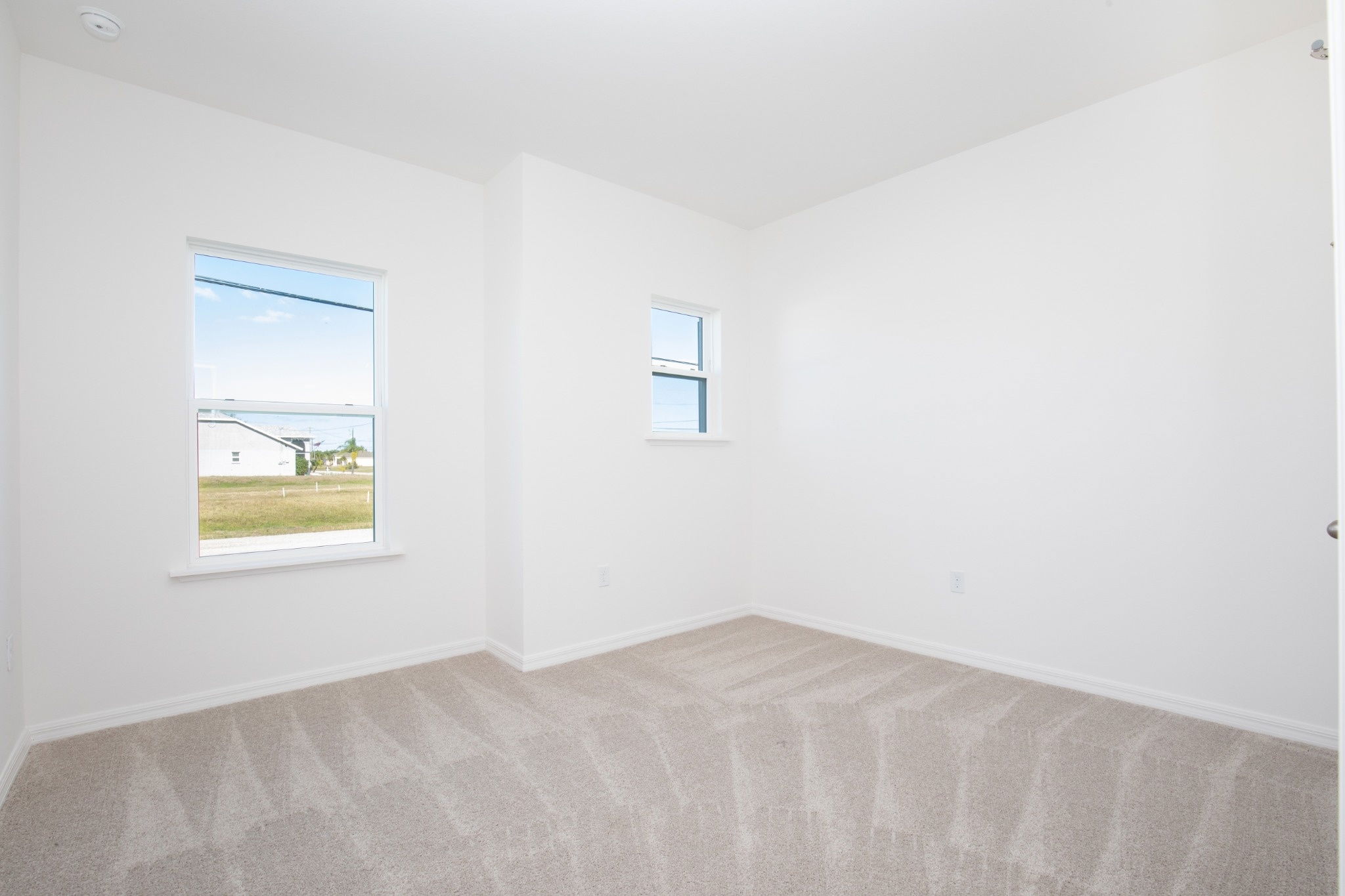 Bright and airy bedroom featuring two windows, neutral-colored walls, and beige carpeting.