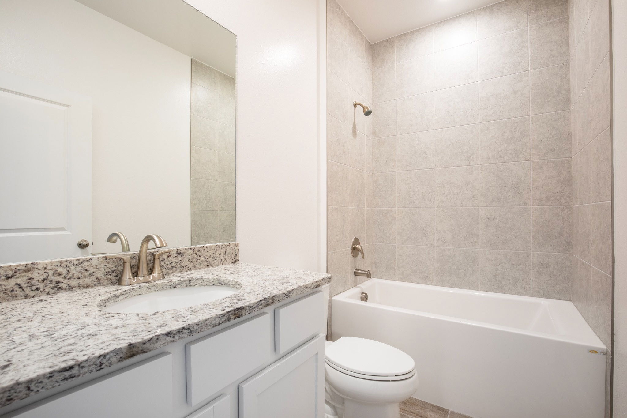 Modern bathroom featuring a granite countertop, a white bathtub, and sleek tile walls.
