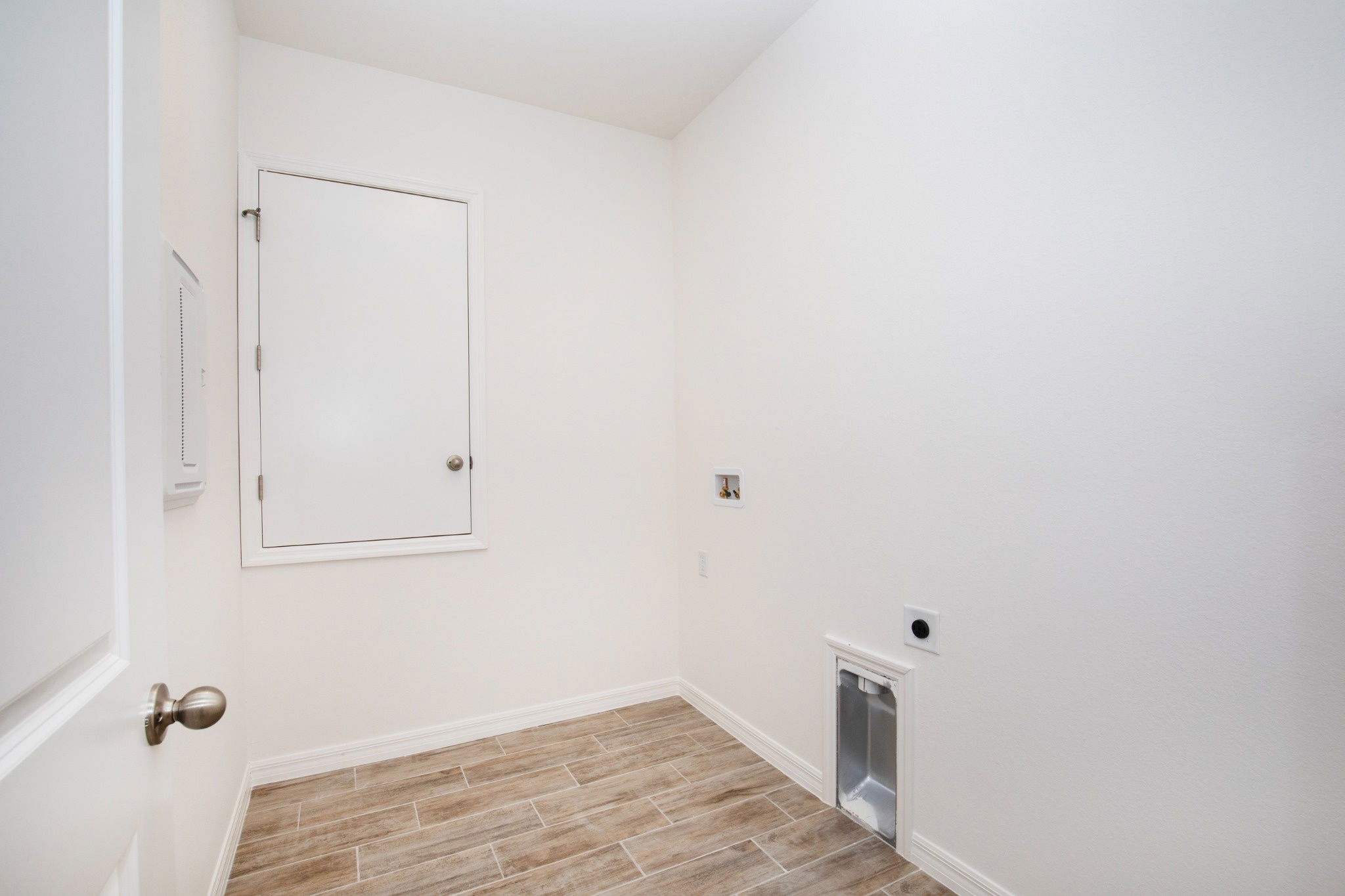 Bright and spacious laundry room featuring tan tile flooring and a white door against a clean, white wall.