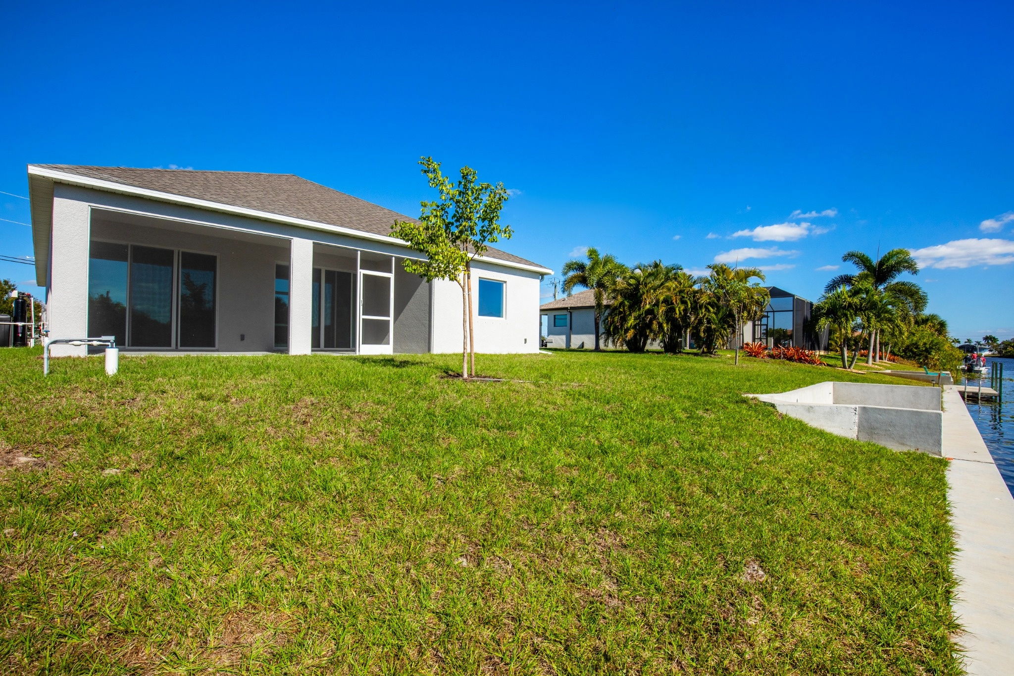 A modern single-family home with large windows and lush green lawn overlooking a waterway under a clear blue sky.