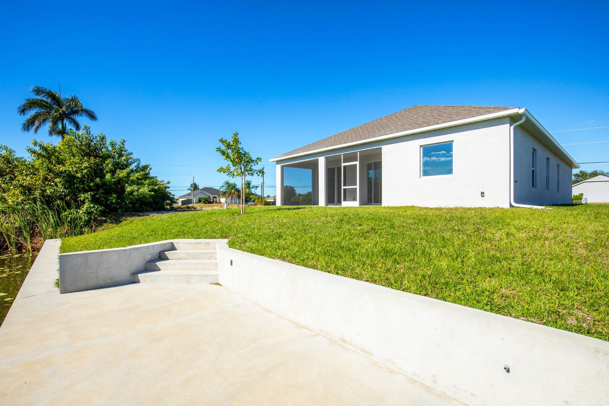 Modern single-family home with a spacious lawn and water access, featuring concrete steps leading to the waterfront.
