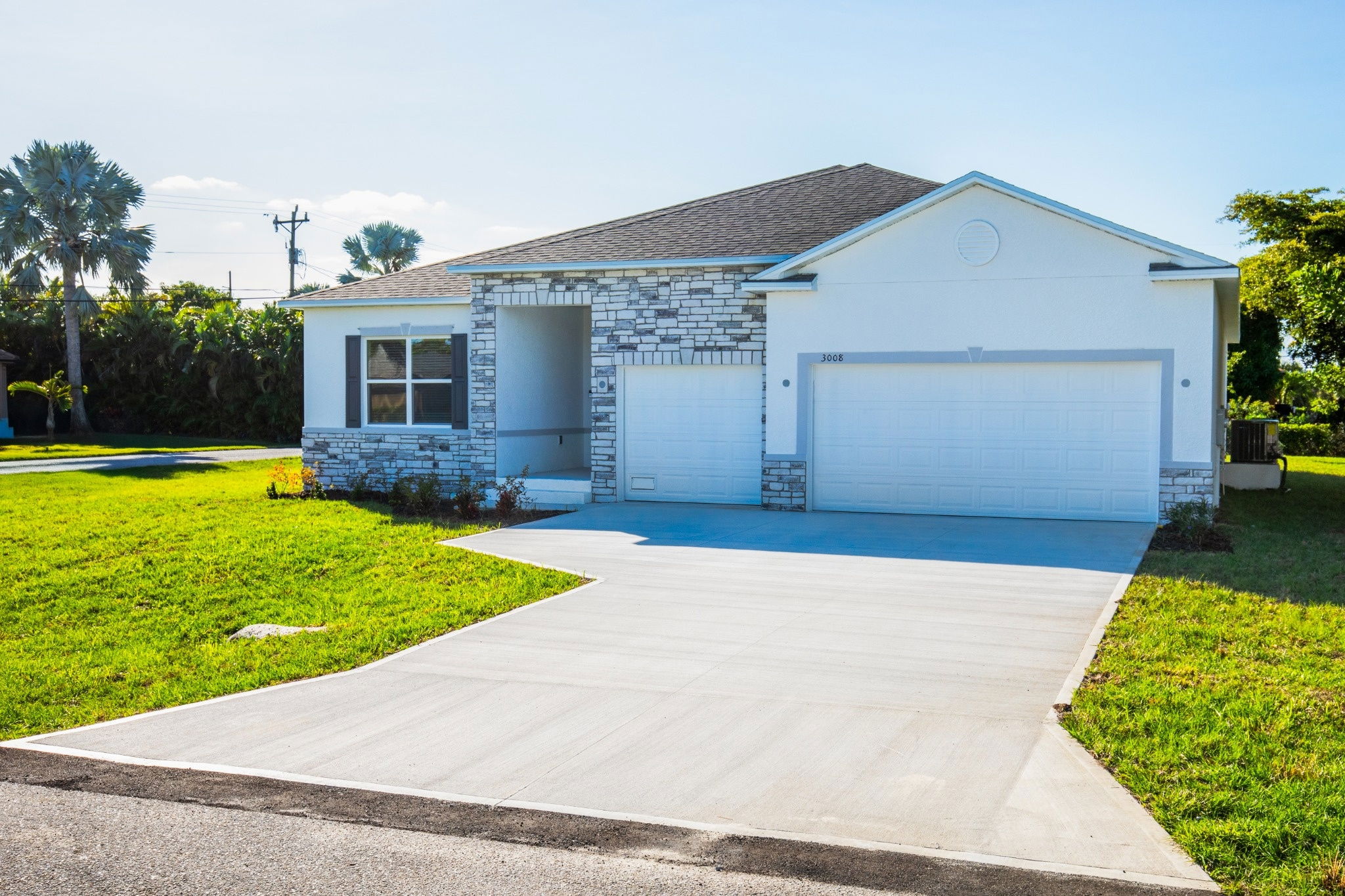 Modern single-family home with a stone facade and spacious driveway surrounded by lush greenery.