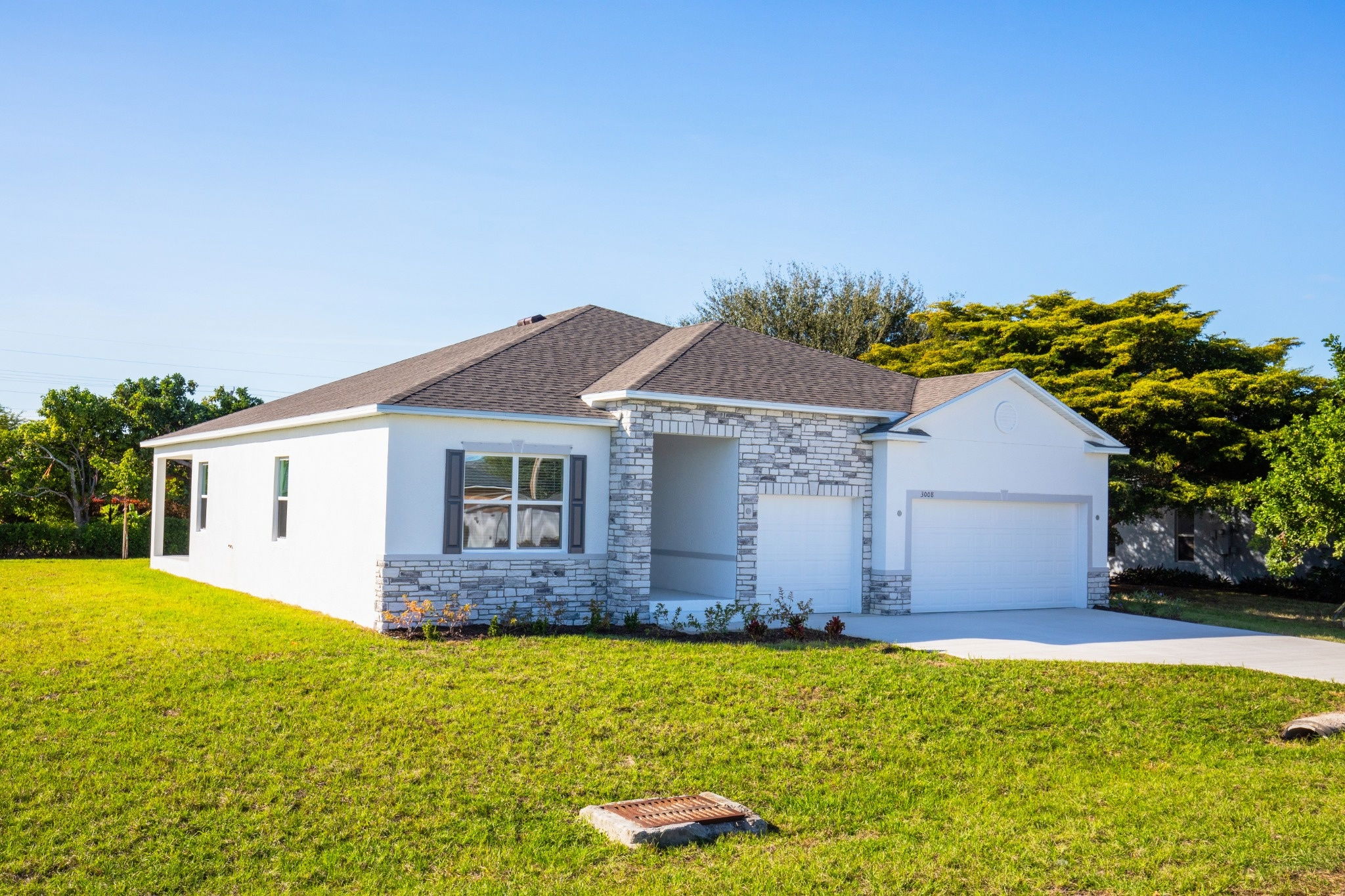 Beautiful modern house with a stone accent facade and a spacious front lawn under a clear blue sky.
