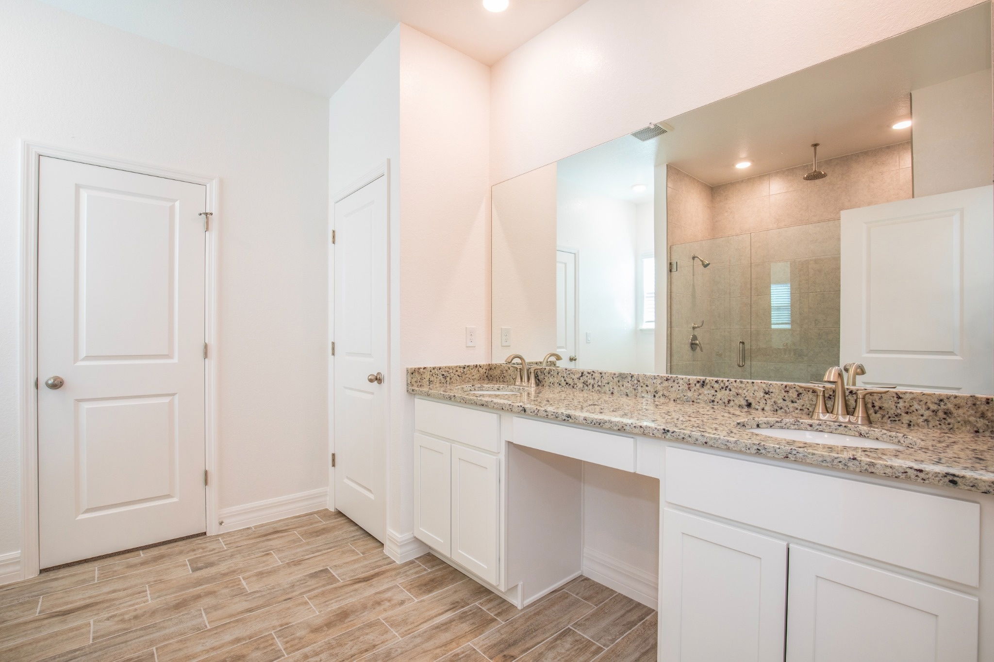 Spacious and modern bathroom featuring a double vanity with granite countertops, white cabinetry, and a glass-enclosed shower.