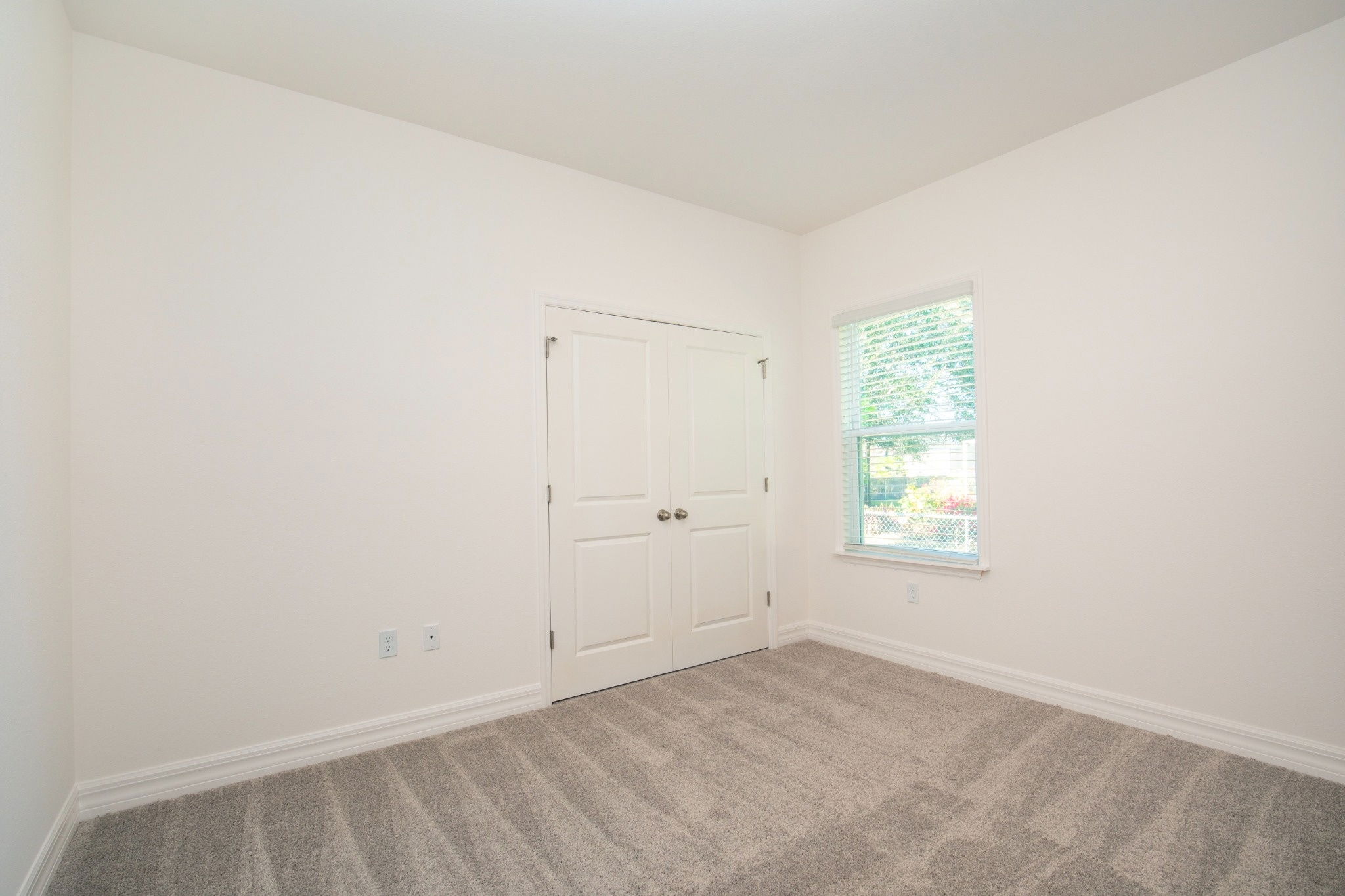 Bright and clean empty bedroom with beige carpet, double doors, and a large window.