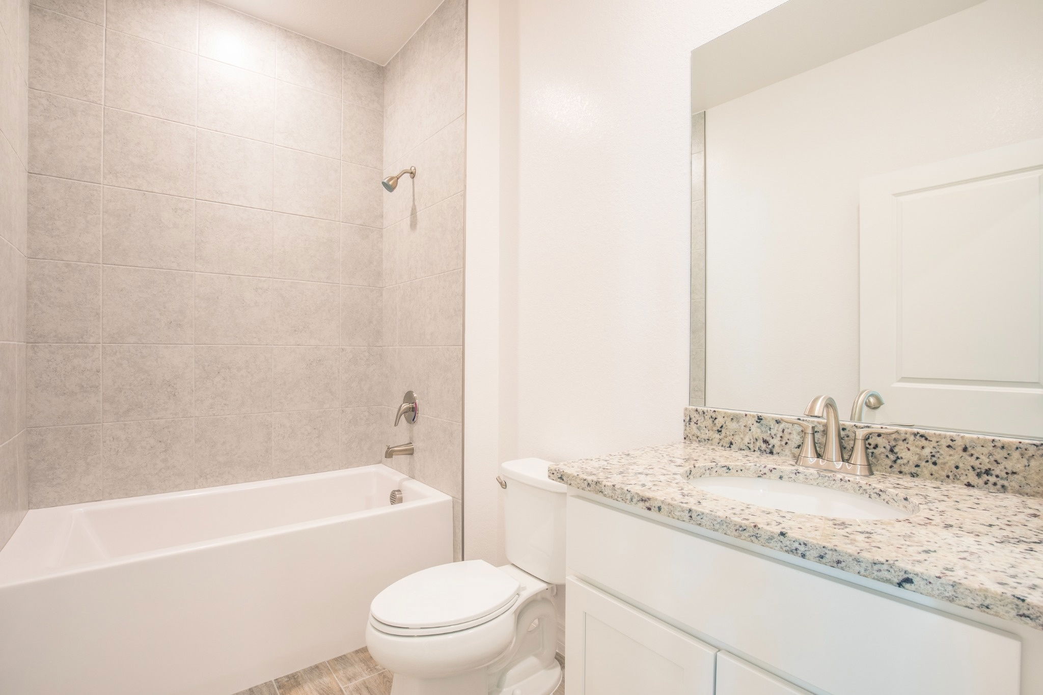 Modern bathroom with a bathtub, tiled walls, and a granite countertop sink featuring a mirror and polished faucet.