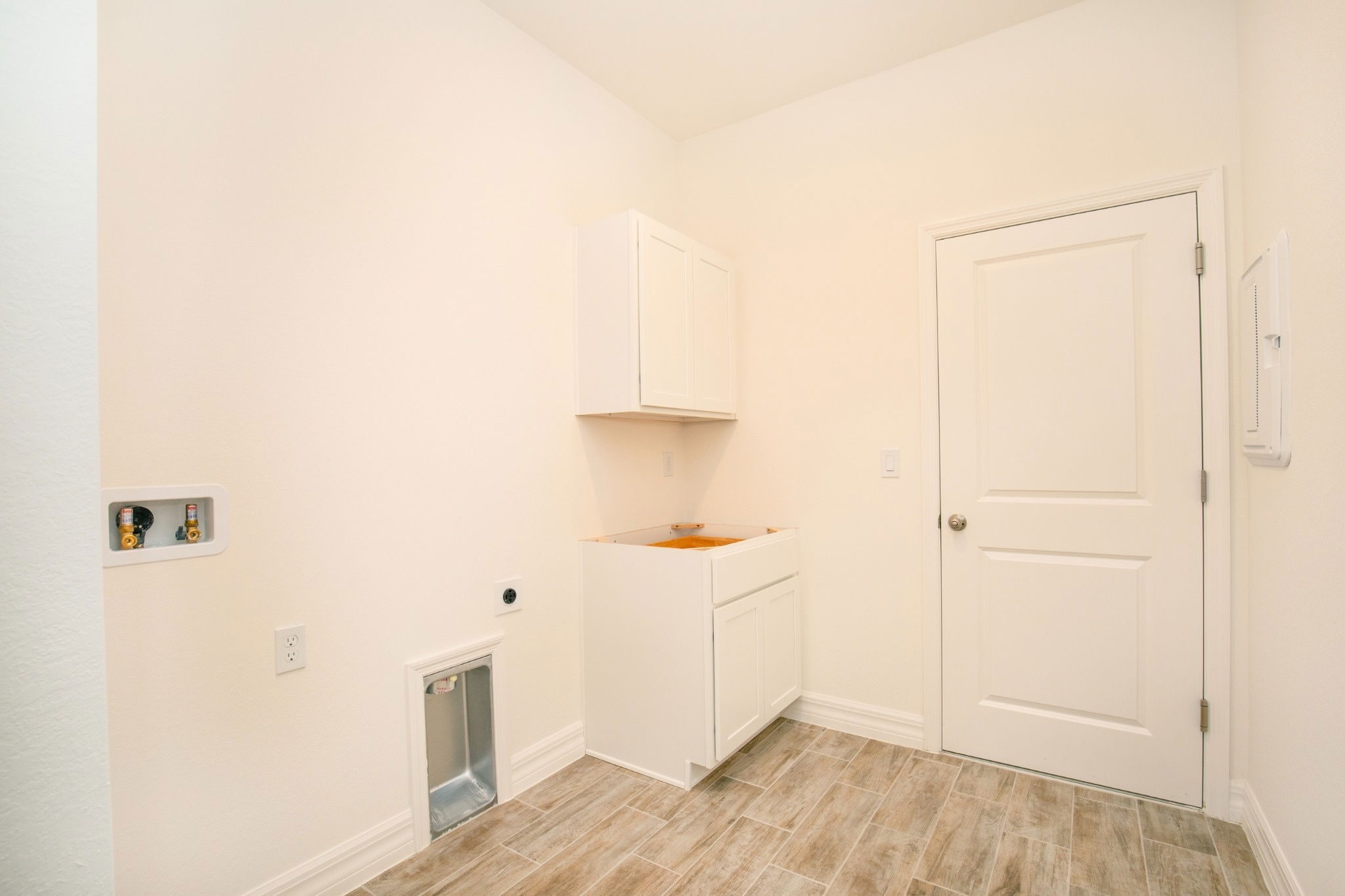 Bright and spacious laundry room featuring white cabinetry, modern tile flooring, and a door leading to the hallway.