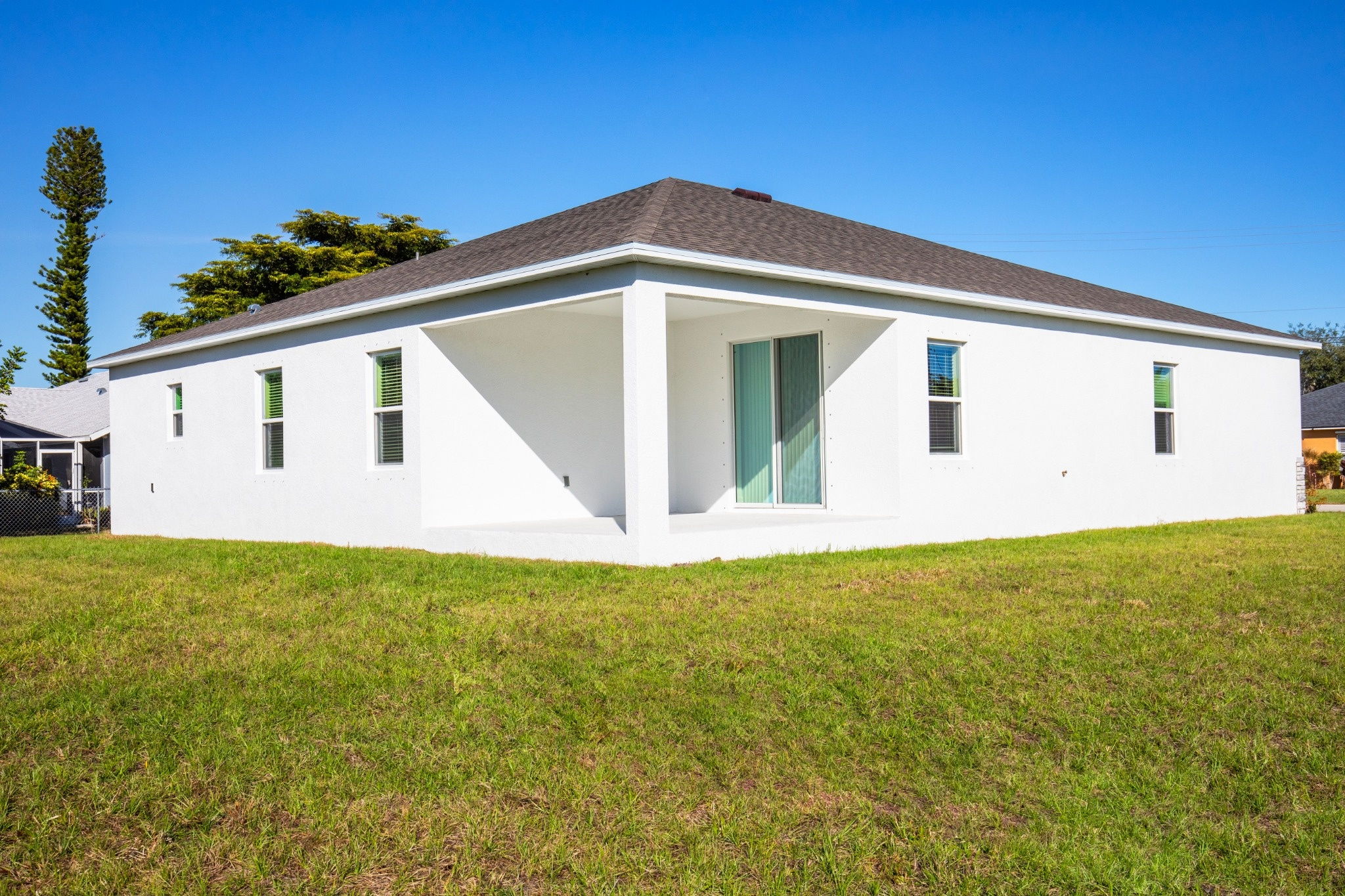 Modern white house exterior with large windows and a well-maintained lawn under a clear blue sky.