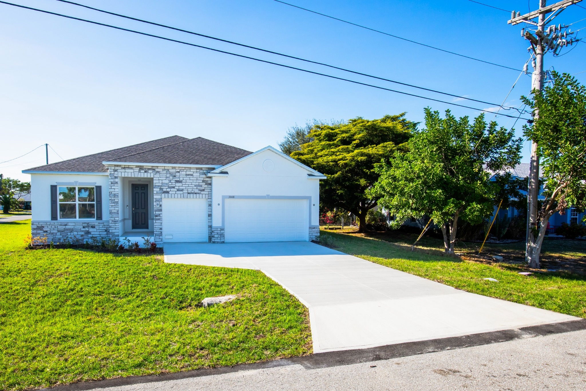 Modern single-family home with stone accents, lush green lawn, and a spacious driveway under a clear blue sky.