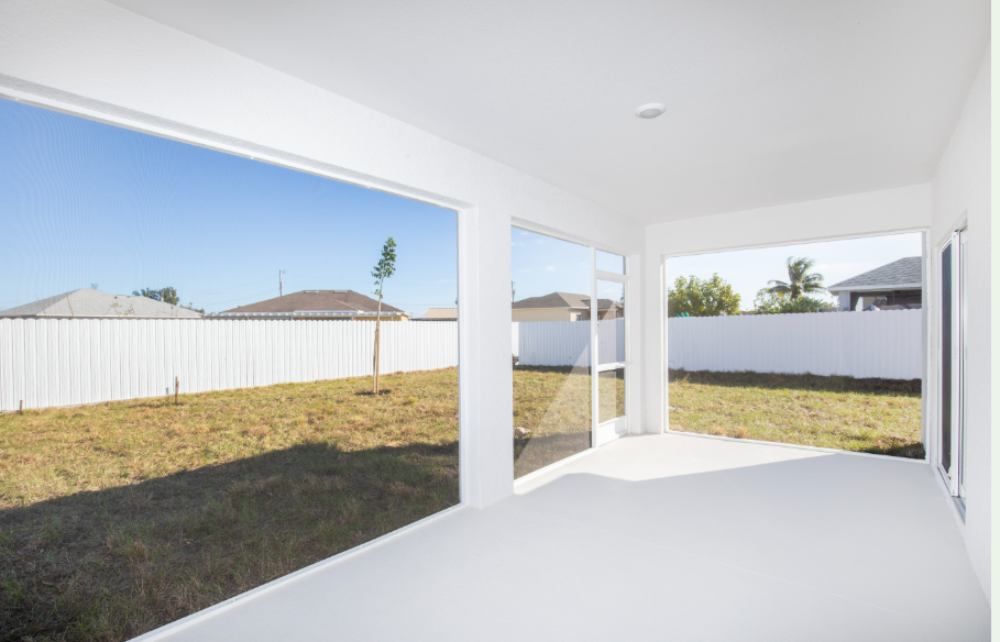 Bright and spacious enclosed patio with large windows overlooking a grassy backyard and clear blue sky.