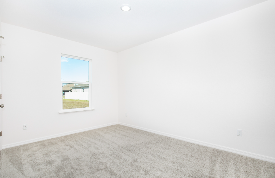 A bright and spacious empty room featuring soft gray carpeting and a window with a view of the outdoor landscape.