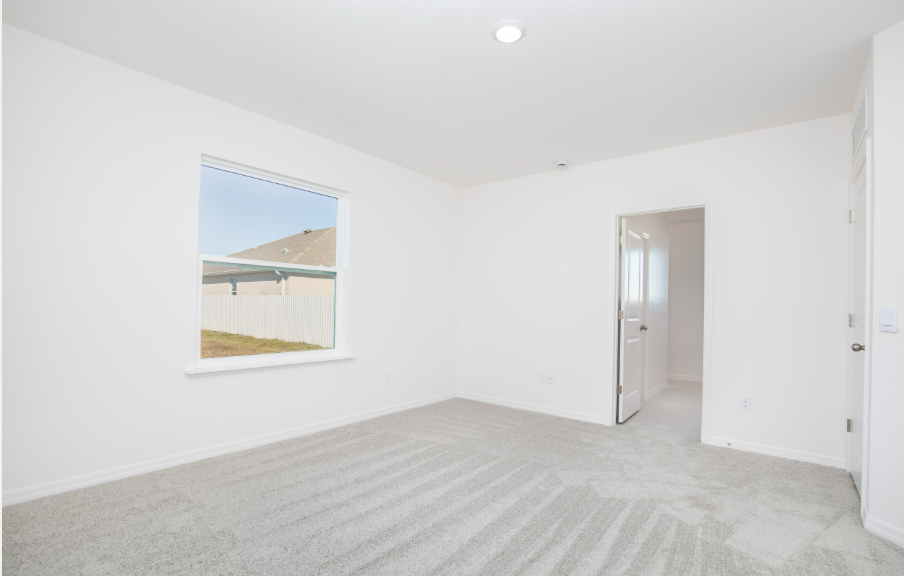 Bright and airy empty bedroom with light-colored walls and a window overlooking a backyard.