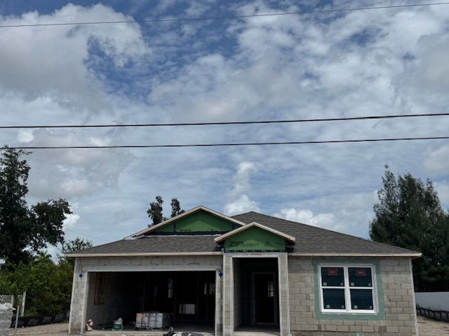Newly constructed single-story house with a gray brick facade under a partly cloudy sky.
