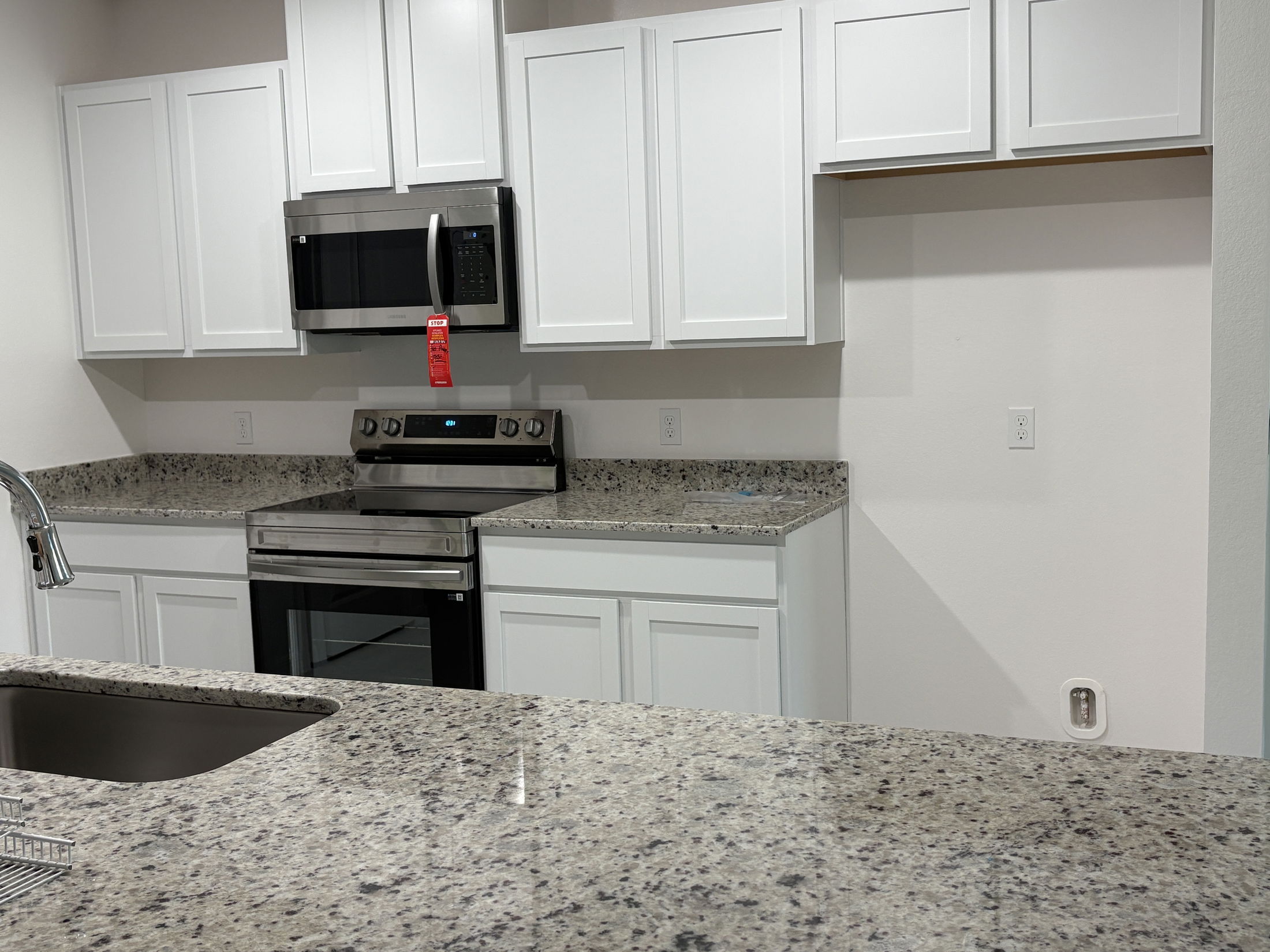 Modern kitchen with white cabinets, granite countertops, and stainless steel appliances, including a microwave and oven.