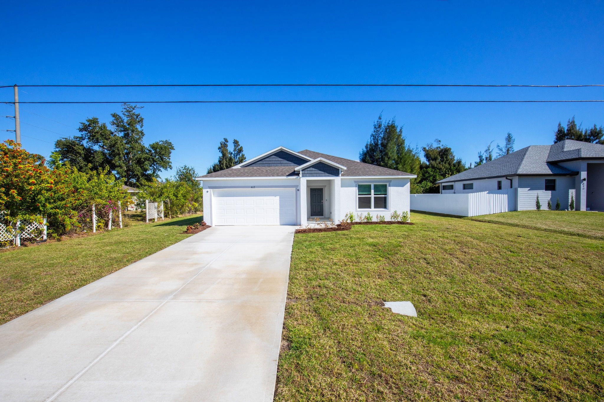 Front exterior view of a modern white house with a driveway and landscaped yard under a clear blue sky.