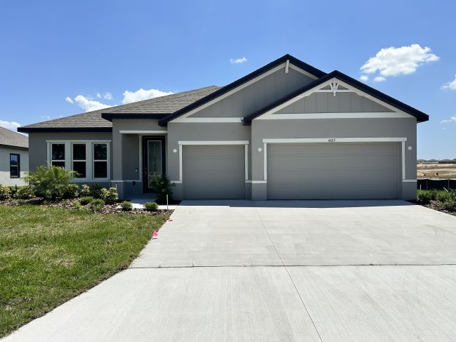Modern single-story home with three-car garage and neatly landscaped front yard under a clear blue sky.