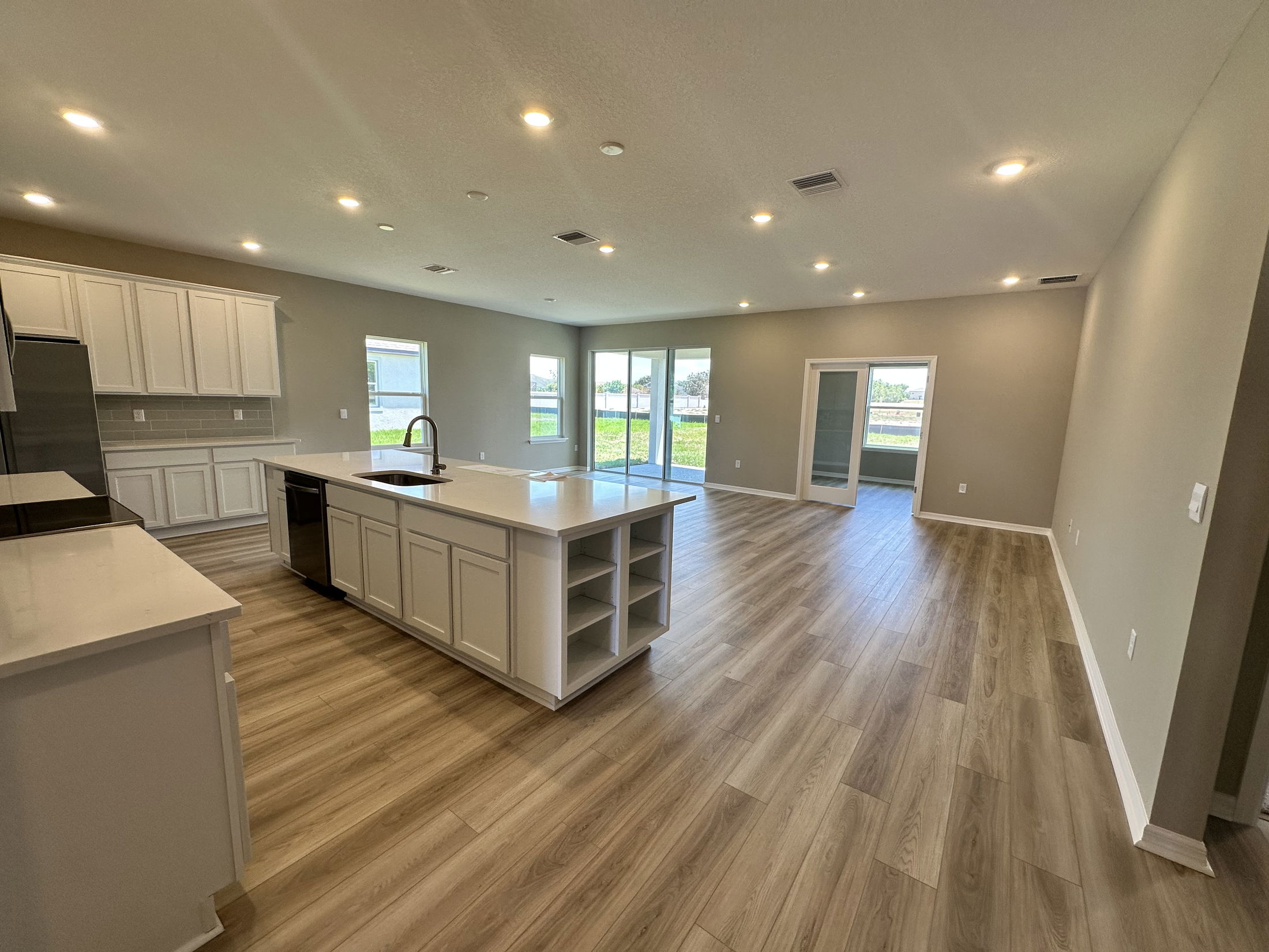 Open-concept kitchen and living area with wood-style flooring and modern white cabinetry leading to a patio with large windows.