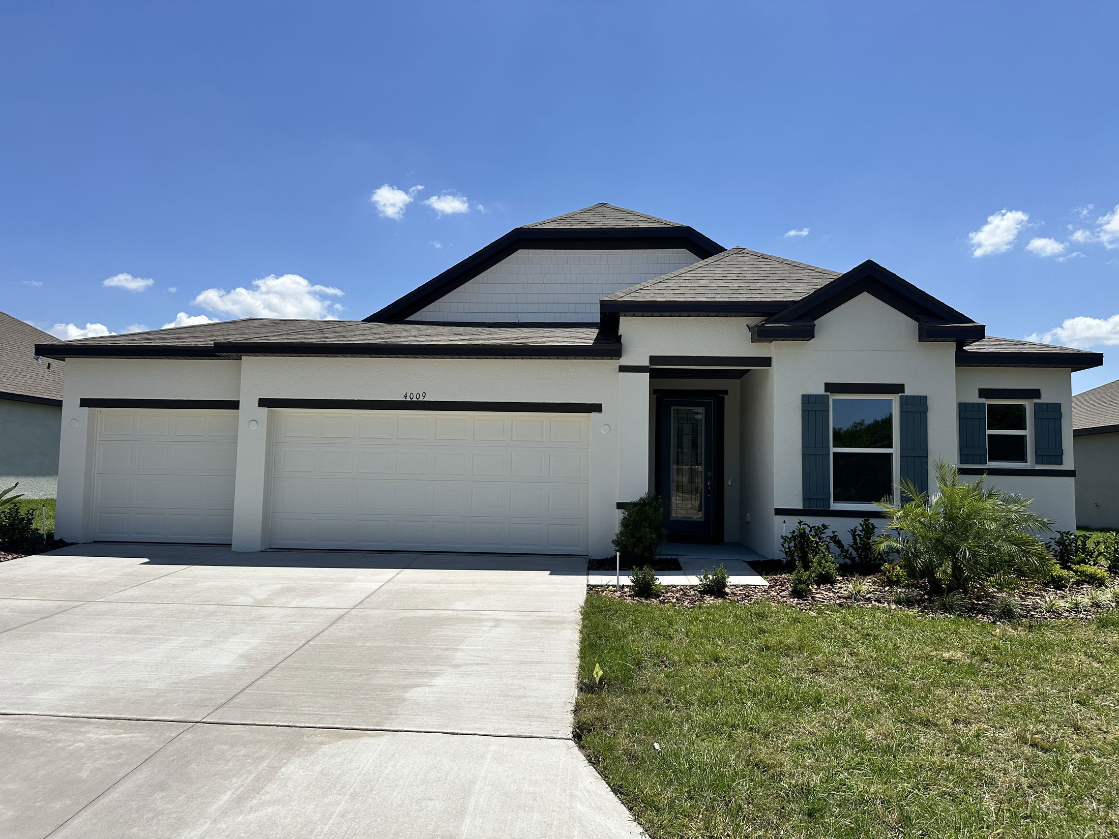 Modern single-story suburban home with a three-car garage and manicured lawn under a clear blue sky.