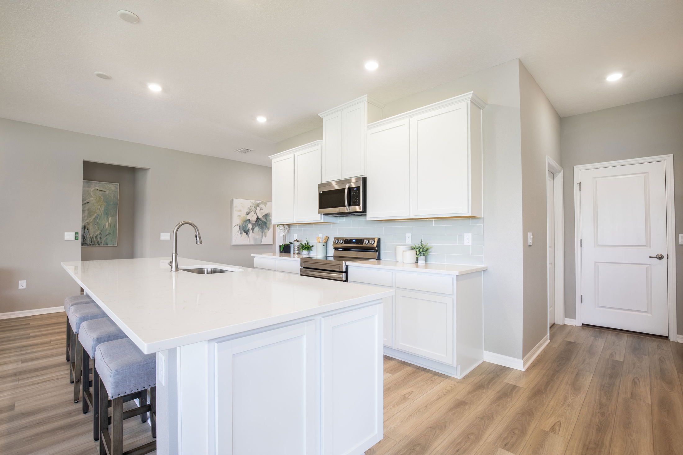 Modern kitchen with white cabinets, stainless steel appliances, and a large quartz island with seating, creating a bright and spacious cooking area.