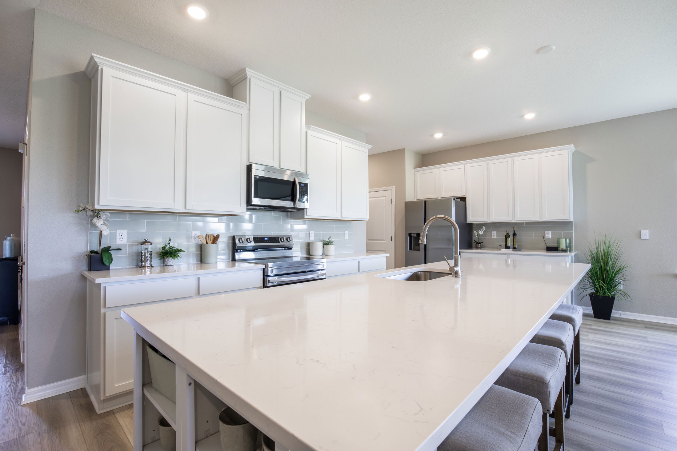 Modern kitchen interior with white cabinets, sleek stainless steel appliances, and a large central island featuring a marble countertop and bar stools.