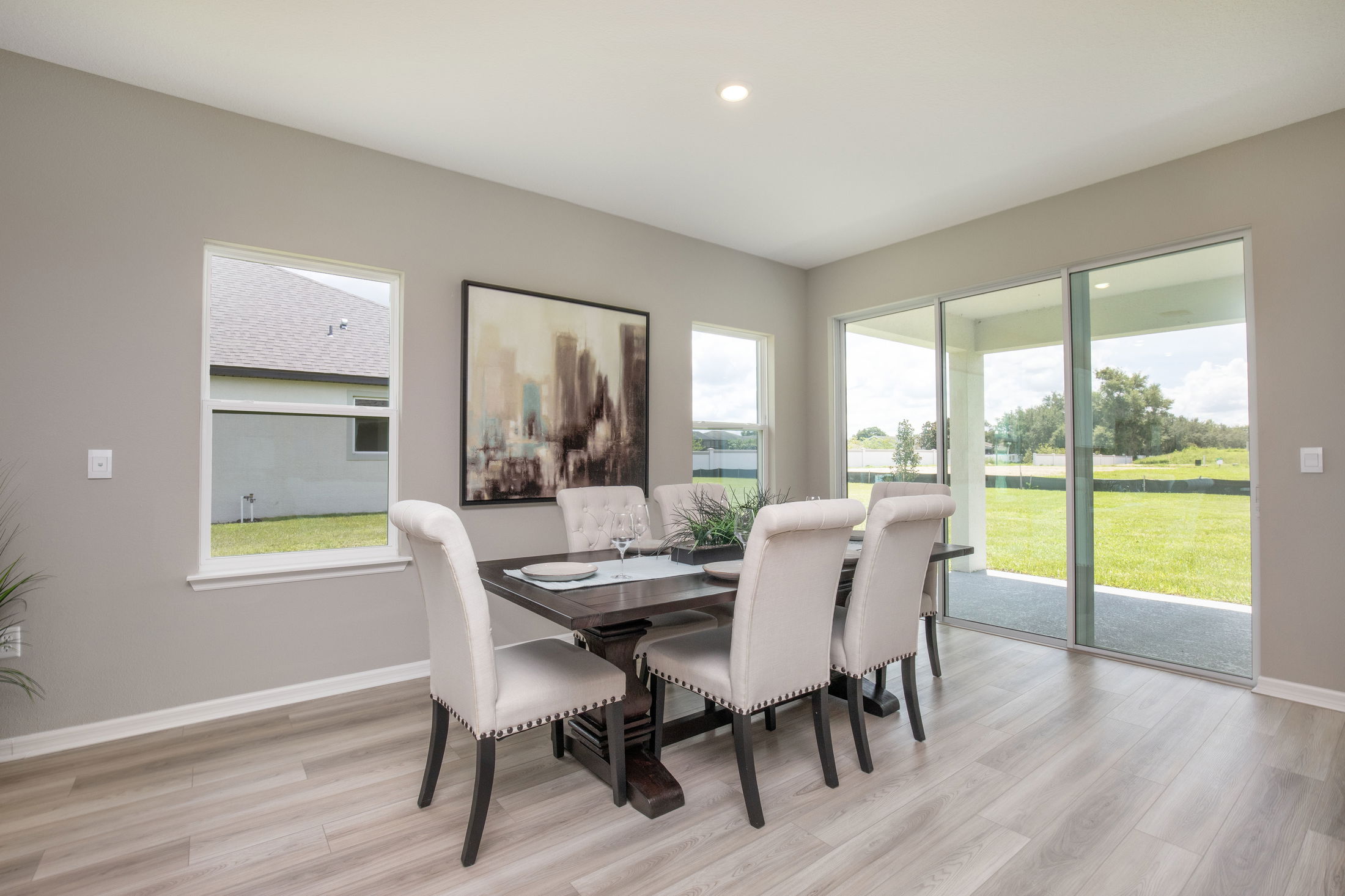 Modern dining room with elegant beige chairs, a dark wood table, large windows, and a scenic outdoor view.