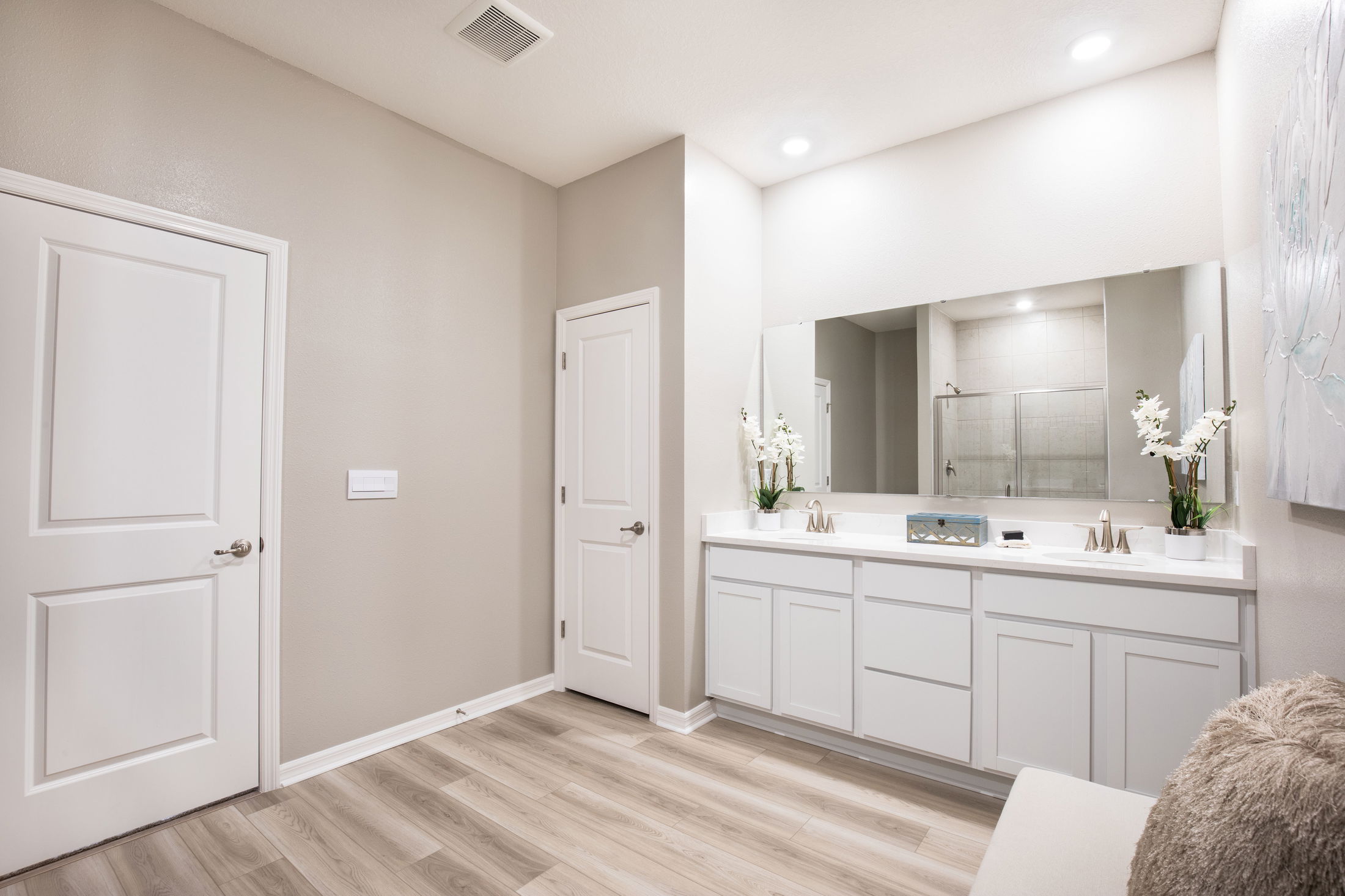 Modern bathroom with double sinks, large mirror, and elegant décor featuring beige walls and wooden flooring.