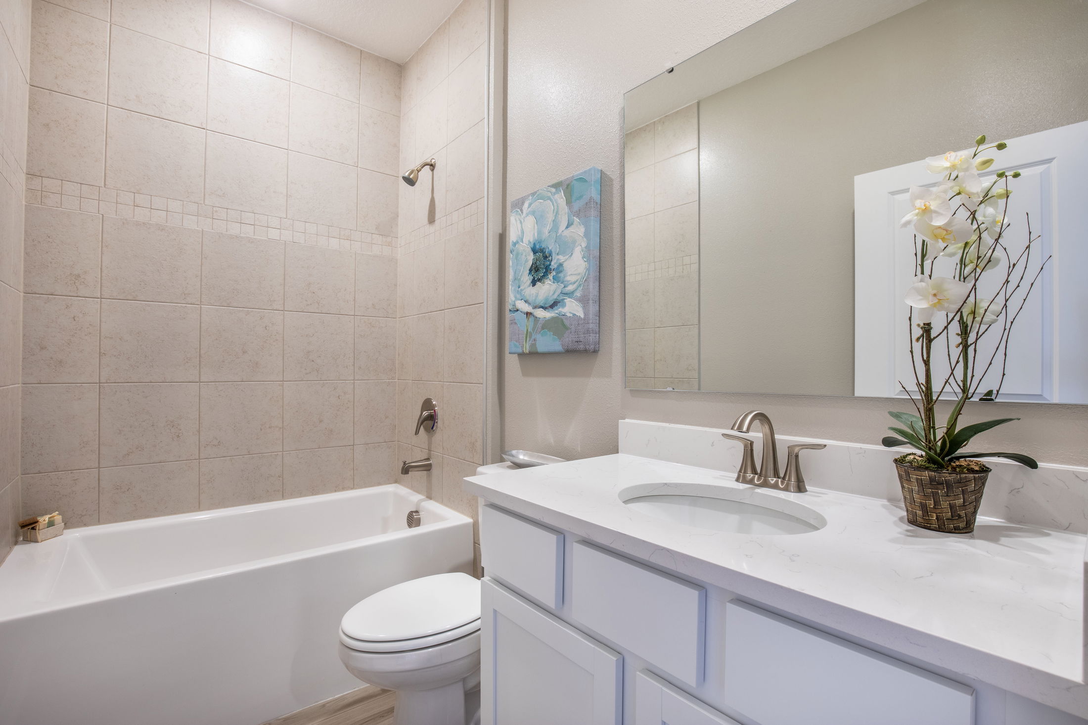 Modern bathroom with a white bathtub, tiled shower walls, a marble-topped vanity, and elegant floral decor.
